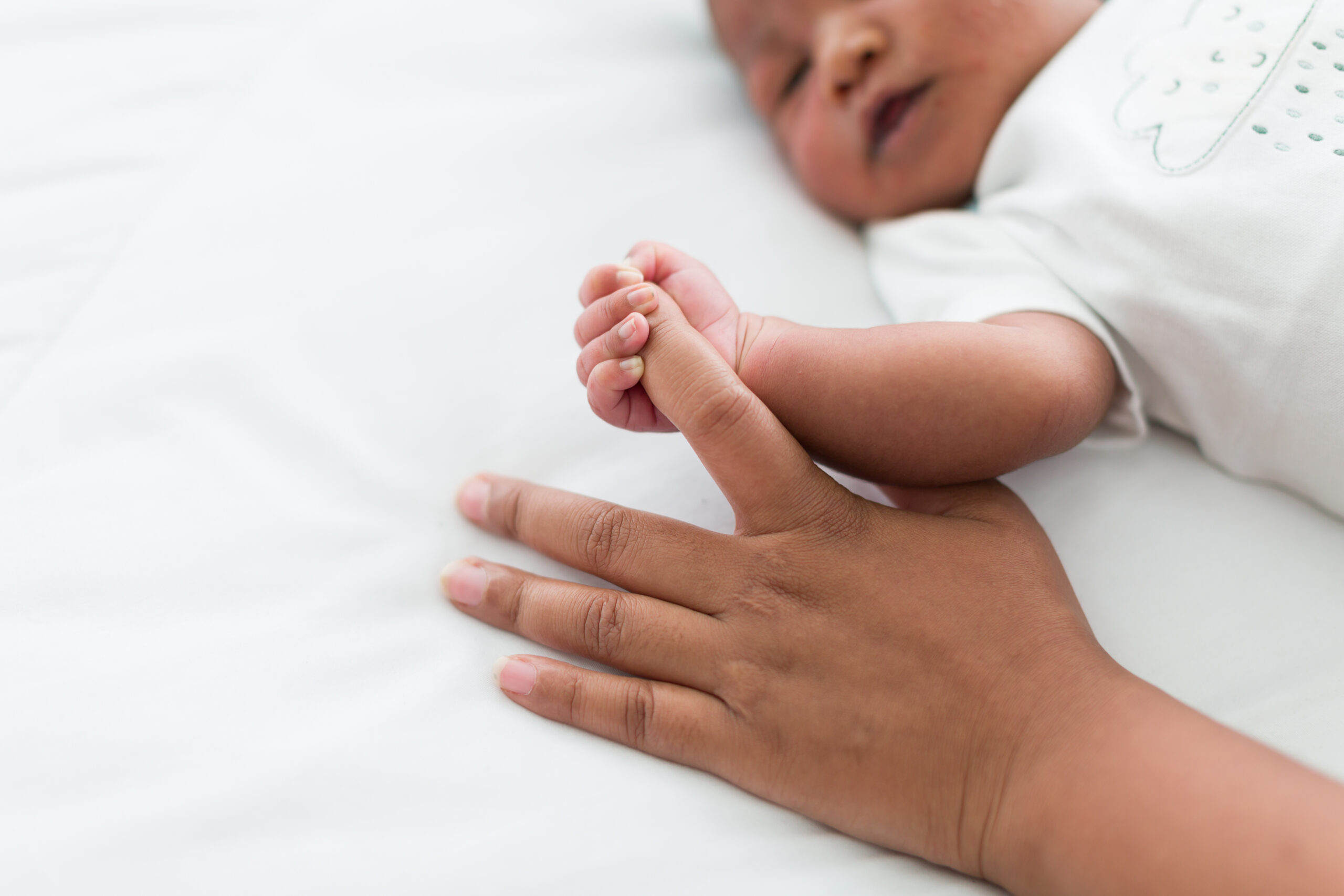 Newborn baby holding motherâs finder and sleeping in blanket on white bed