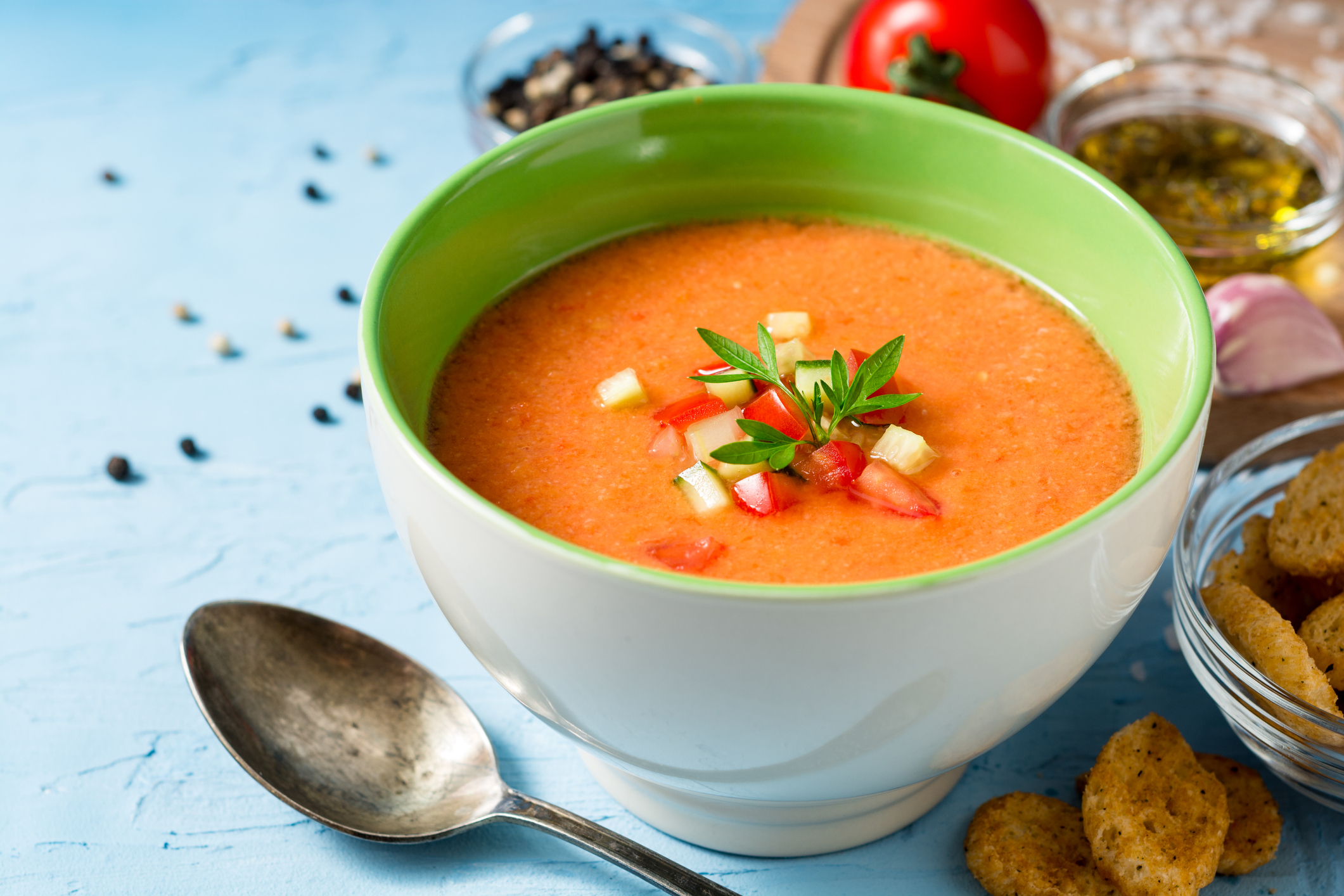 Summer cold soup gazpacho with parsley and vegetables on blue concrete background.