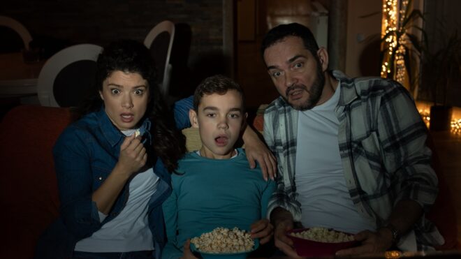 Family of three, father, mother and son, watching horror movie in livingroom in dark.