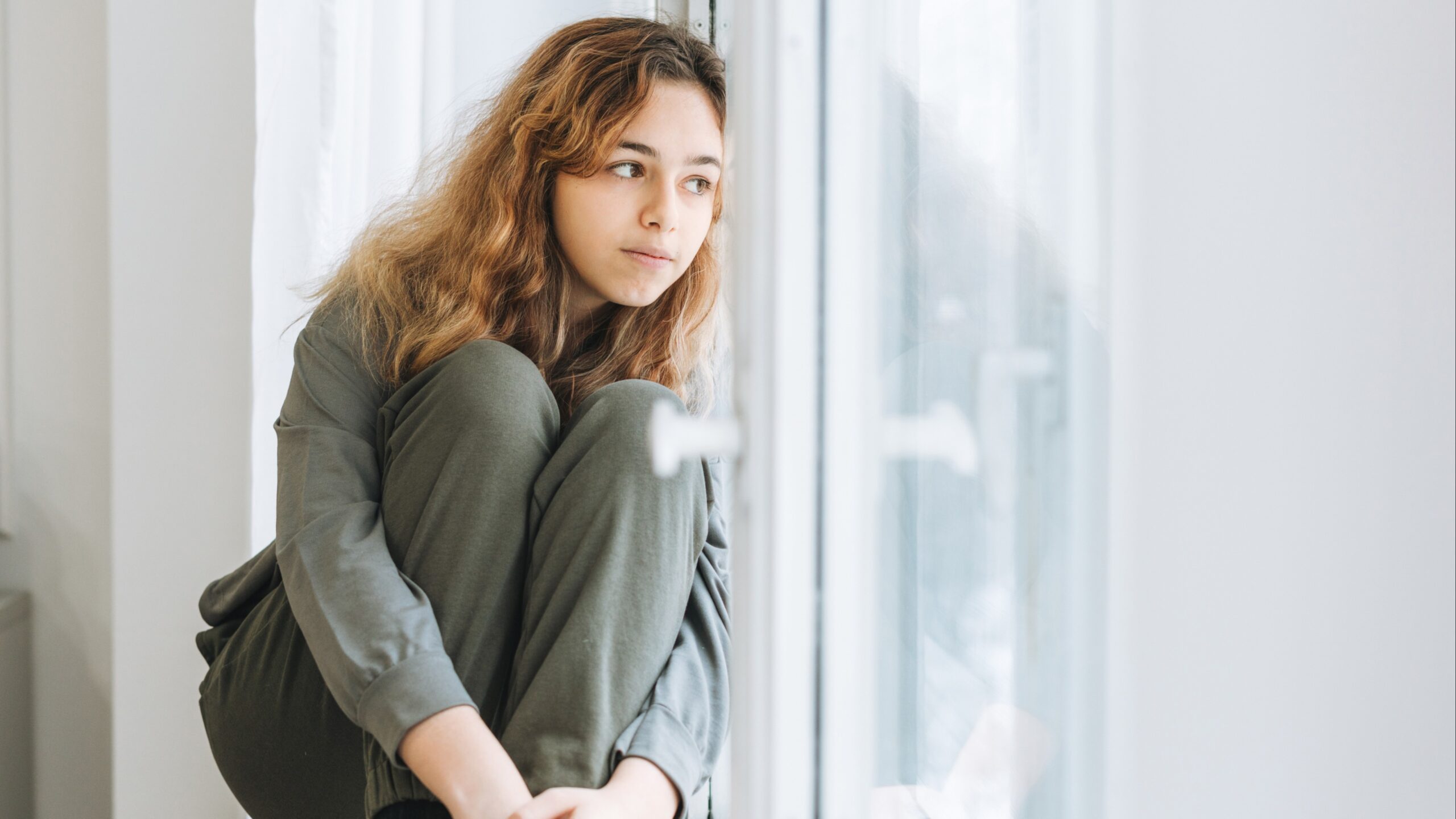 Sad teen by window- Signs your teen may be at risk for suicide