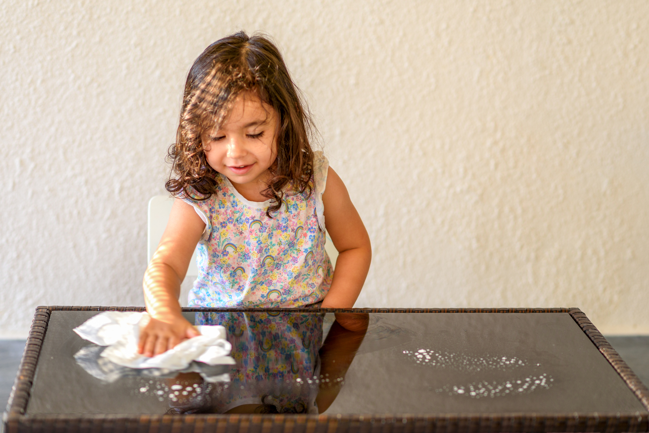 Cute child help mom cleaning glass table. Little girl make cleaning in room at home.