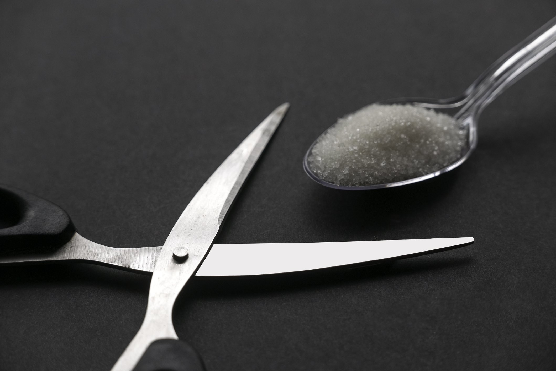 Scissors and a white sugar in a transparent spoon on black background.