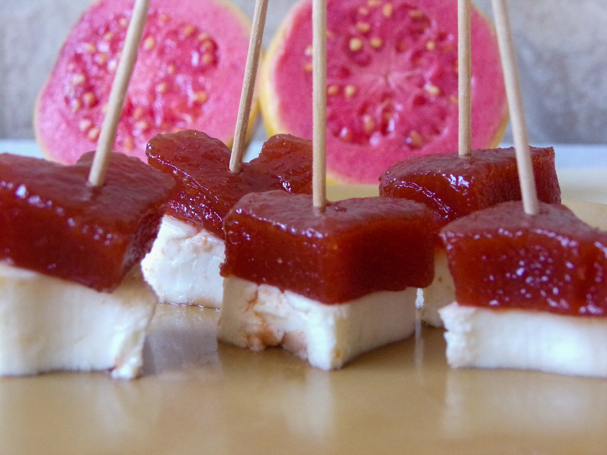 Brazilian dessert Romeo and Juliet, goiabada jam of guava and cheese Minas. Yelow background. And two sliced guavas composing the scene.