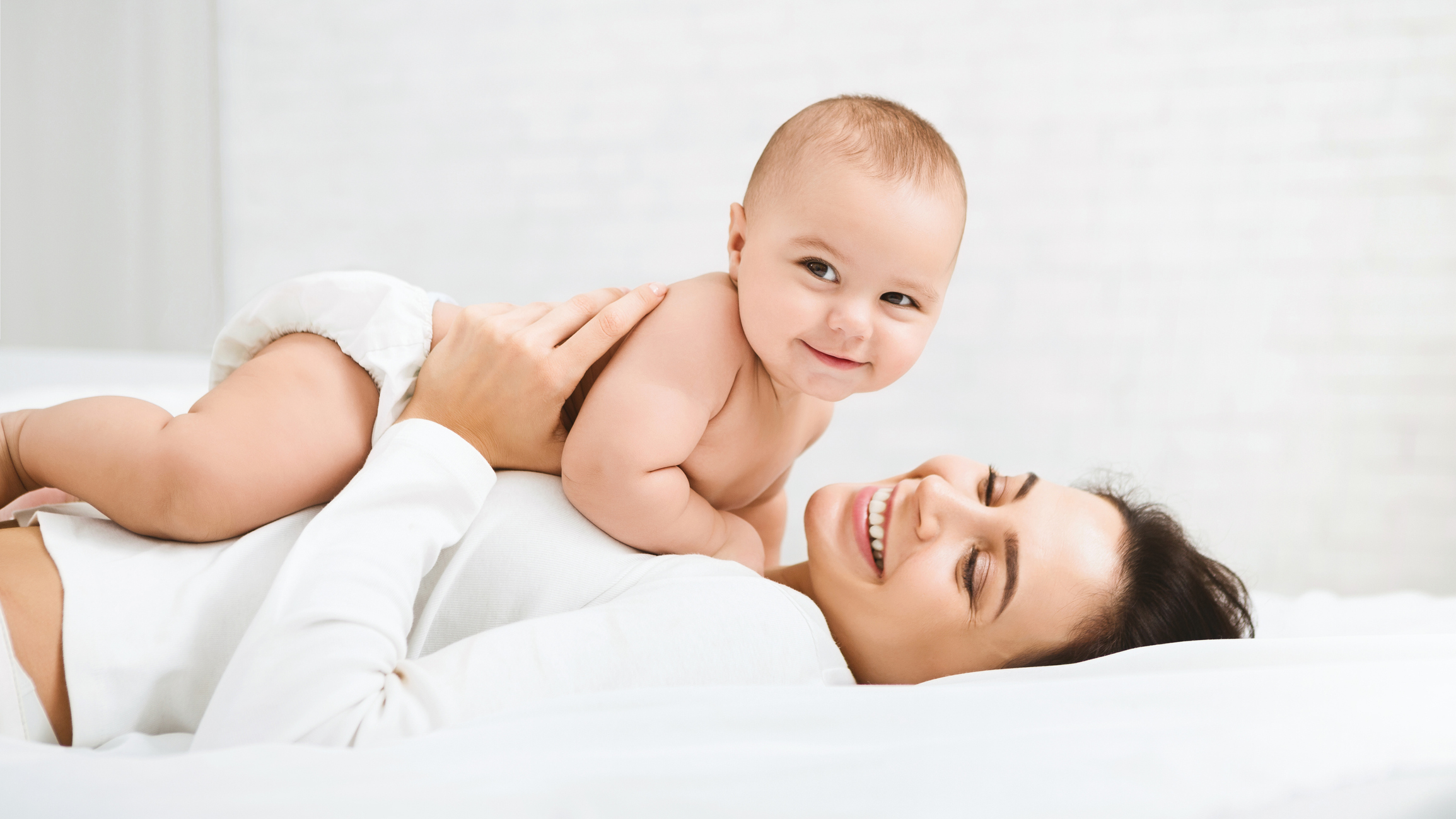 Mom and baby boy in diaper playing in bedroom