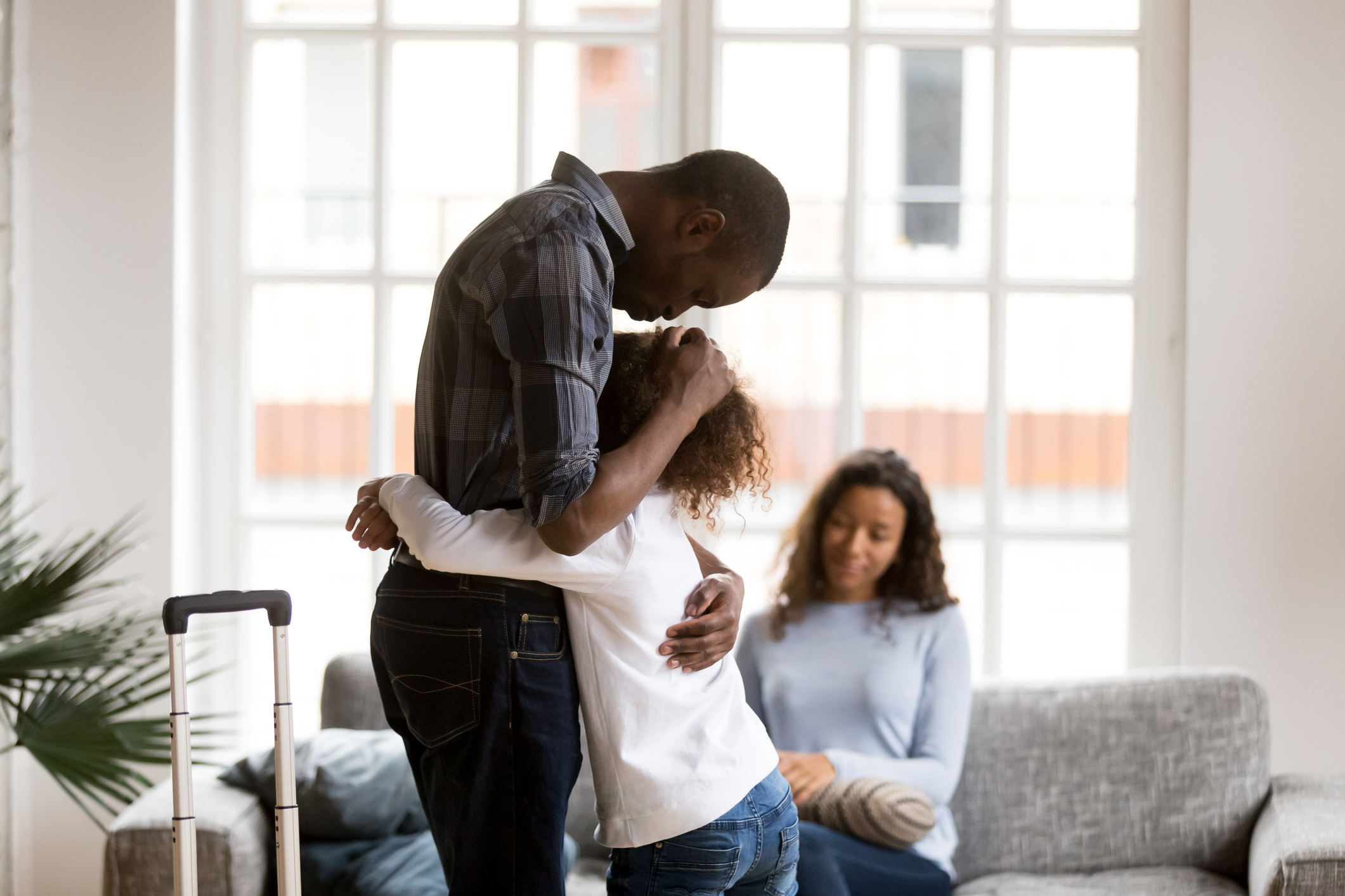 Sad African American girl hug dad leaving home with suitcase