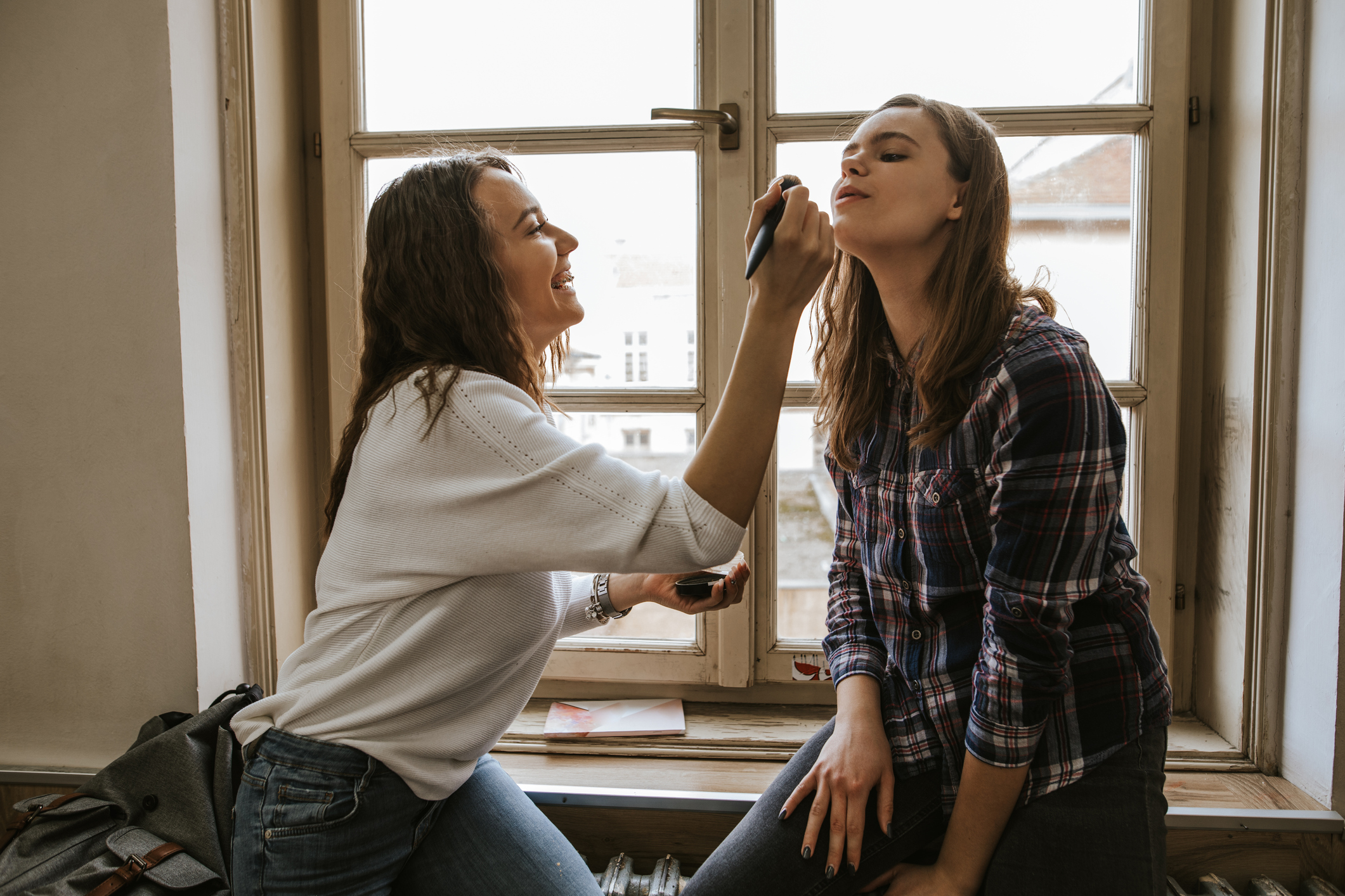 Two teenage girls make up in classroom near window