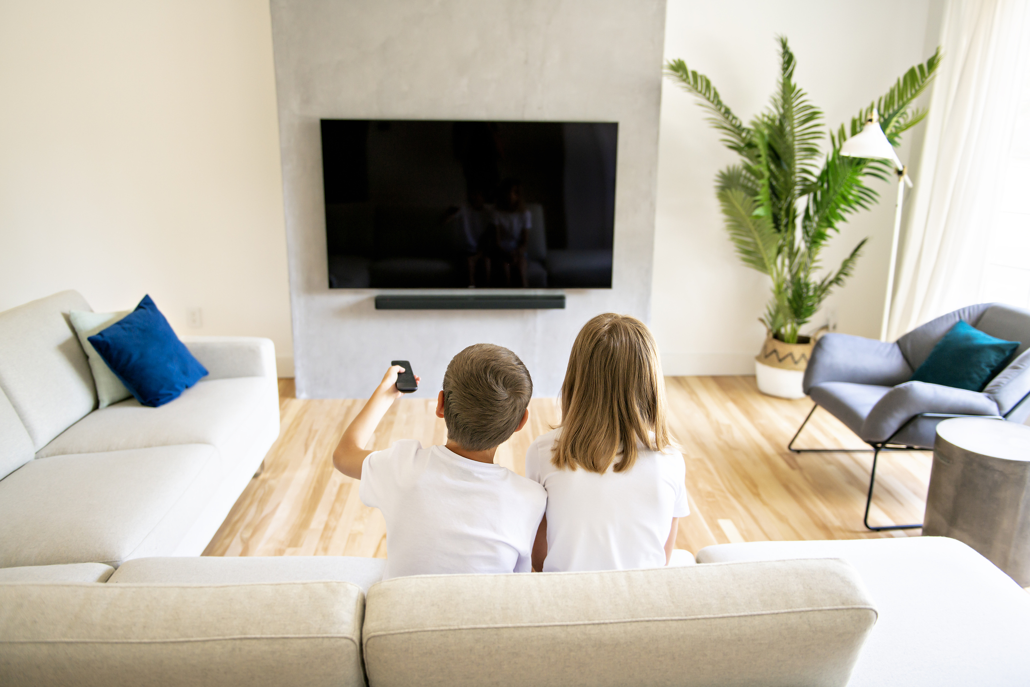 A two family brother and sister holding remote control and watching TV show. Back view