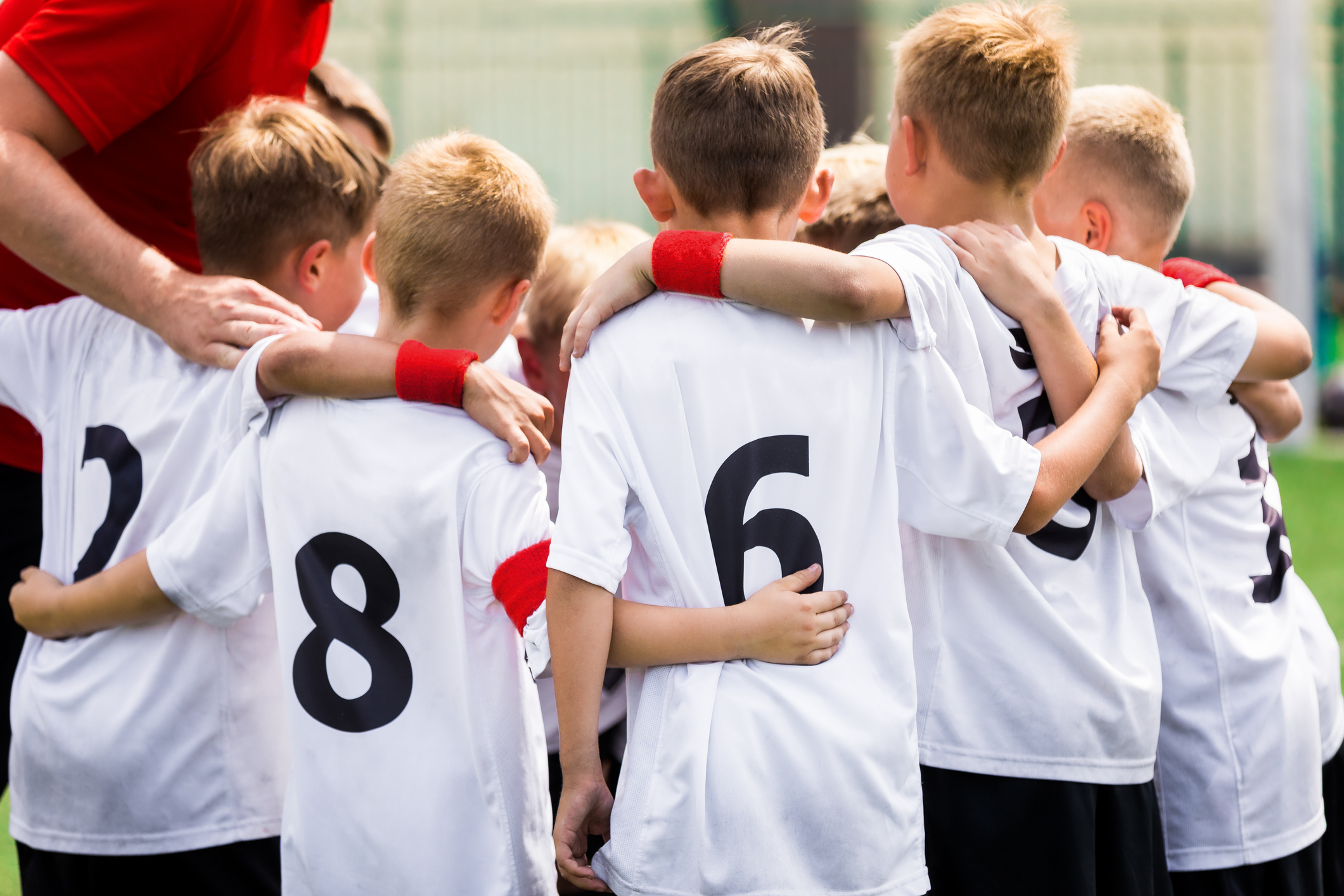 Junior soccer football team stacking hands with coach before a match. Image of junior sports team with young coach. Coaching Kids Team Sports