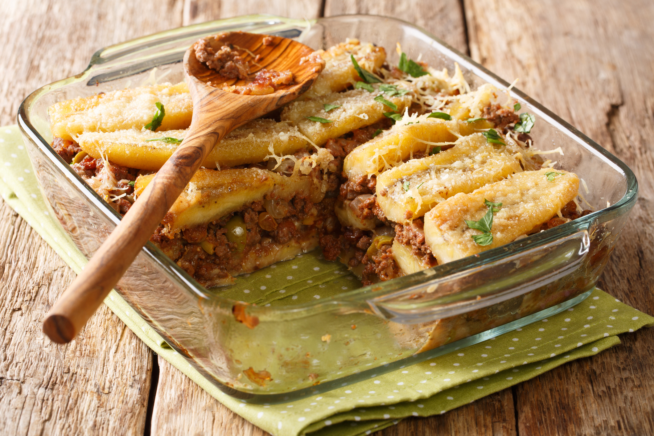 Cutting out a piece of lasagna Puerto Rican pastelon close up in baking dish. horizontal