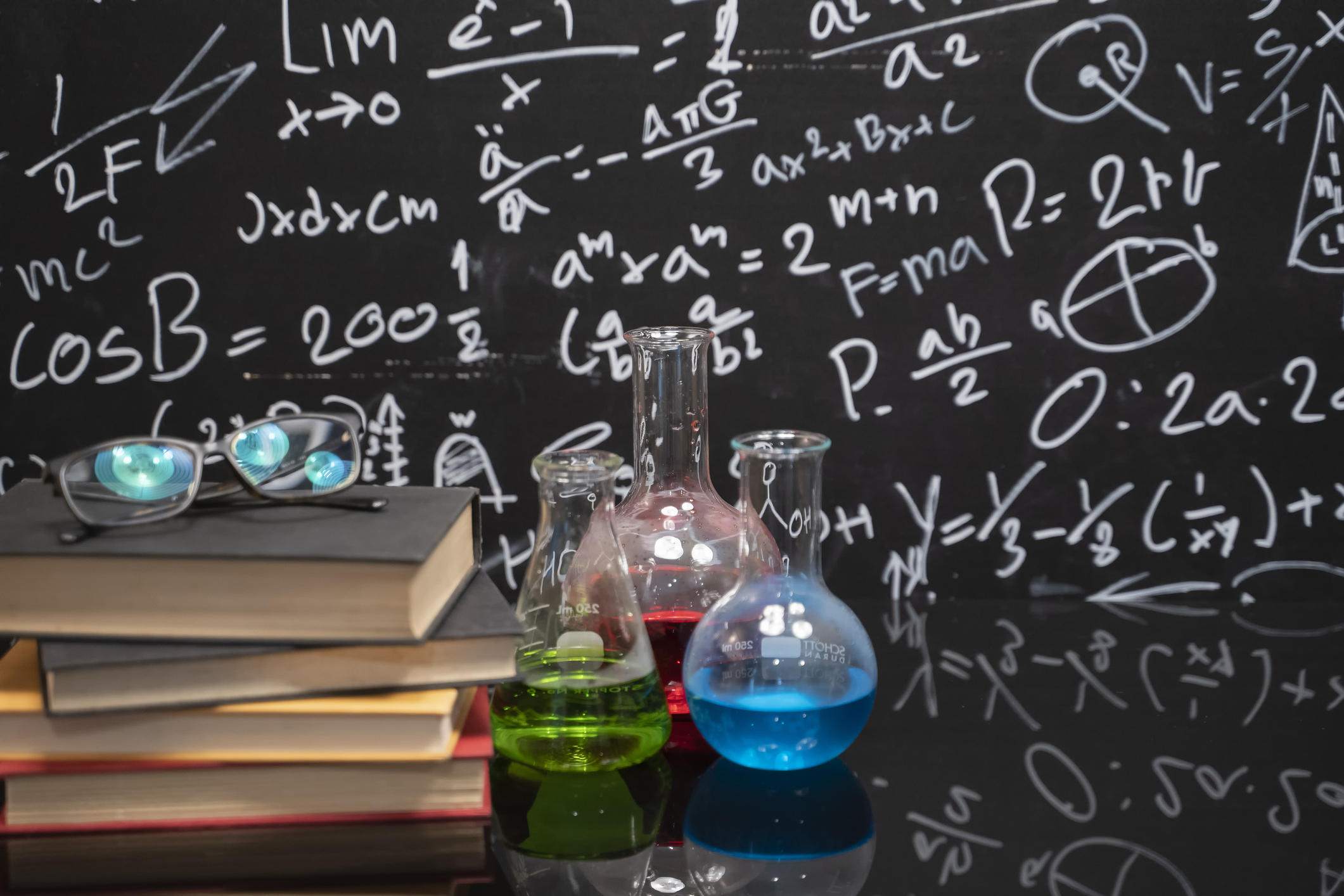 Glasses on old books and experiment bottle on a black table with a blackboard on the background.