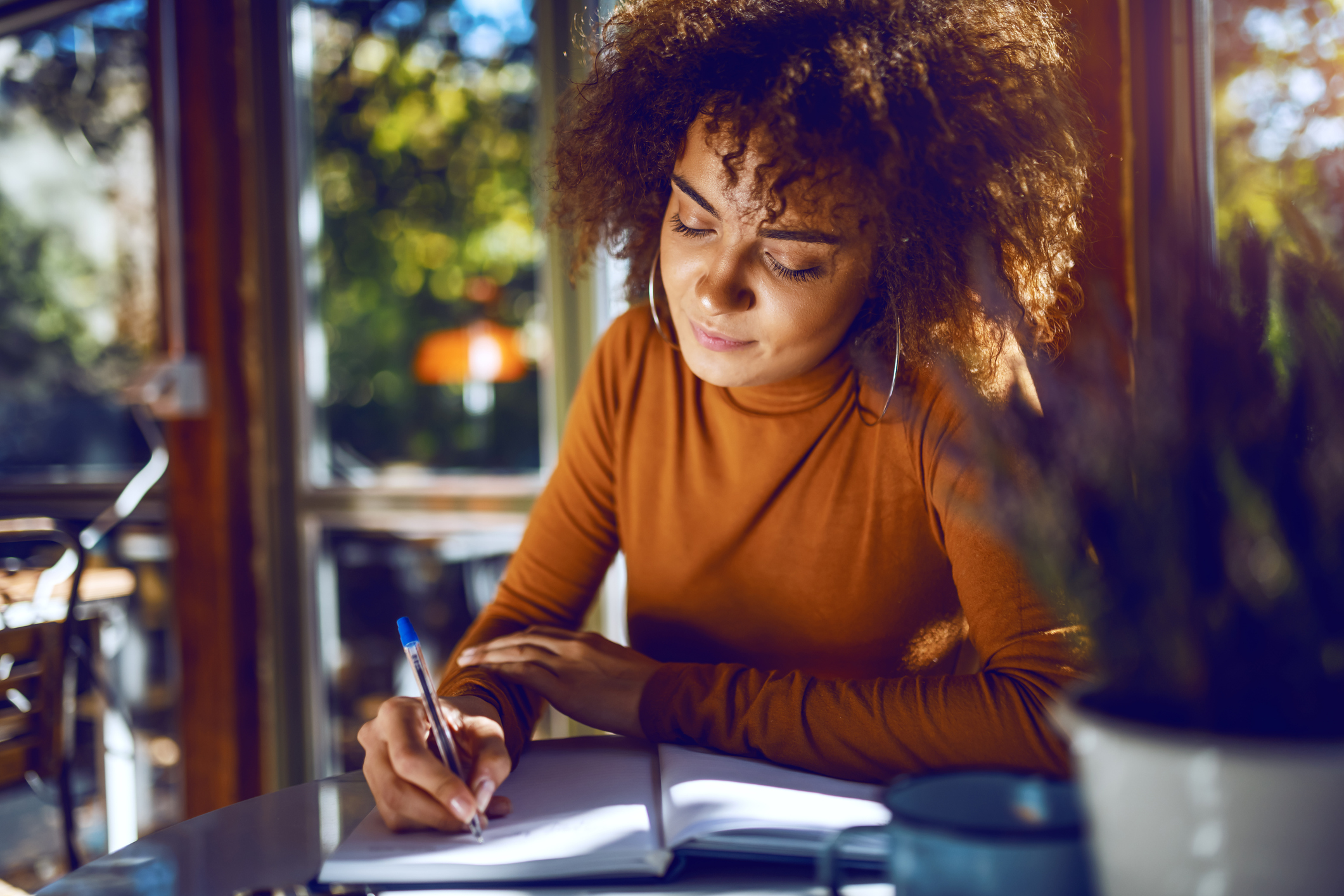 Portrait of cute mixed race student with curly hair and in turtleneck sitting in cafe and studying for exams.