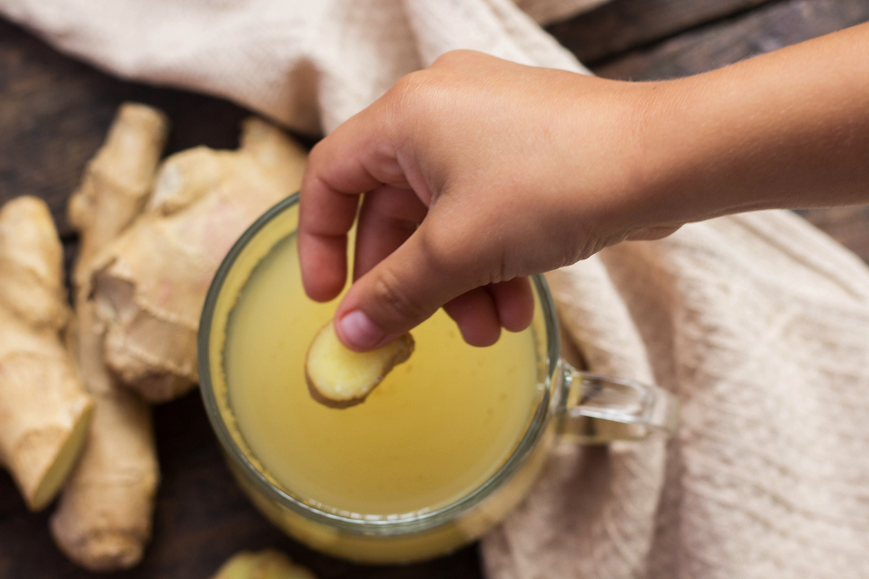 Cup of ginger tea on wooden background and woman hand