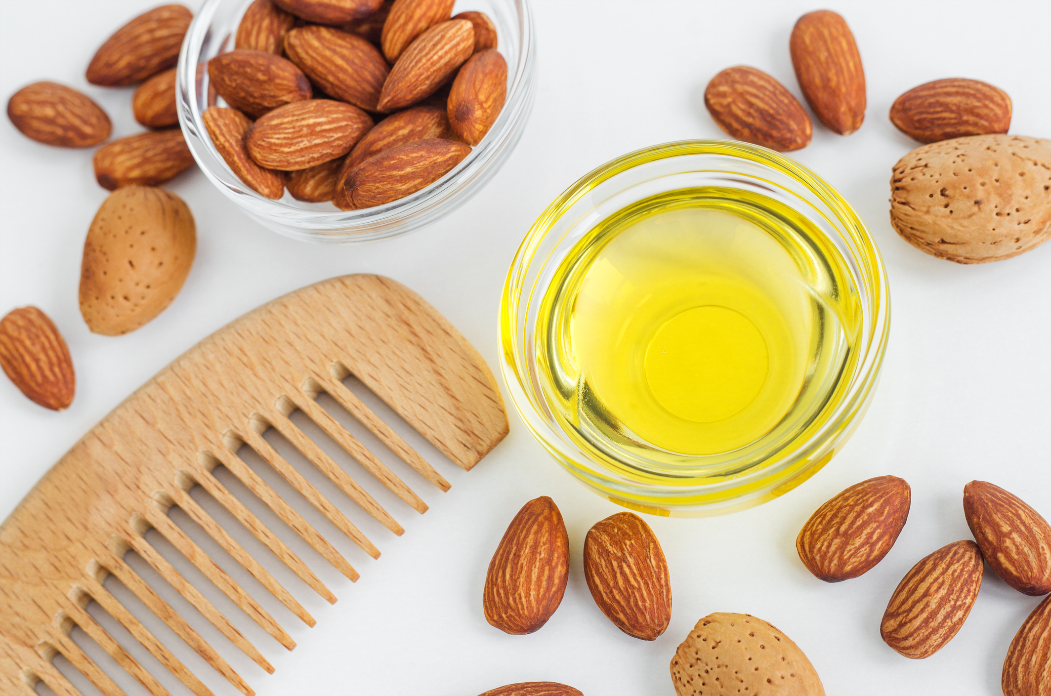 Small glass bowl with almond oil and wooden hairbrush for natural hair care. Top view, copy space.