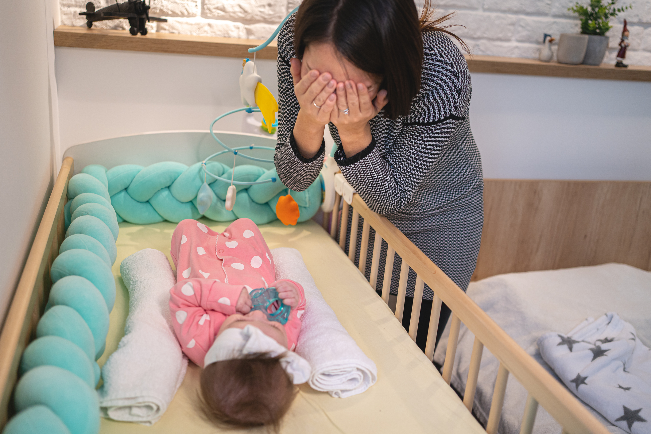 Single mother playing peekaboo with her baby girl while she lying in a crib