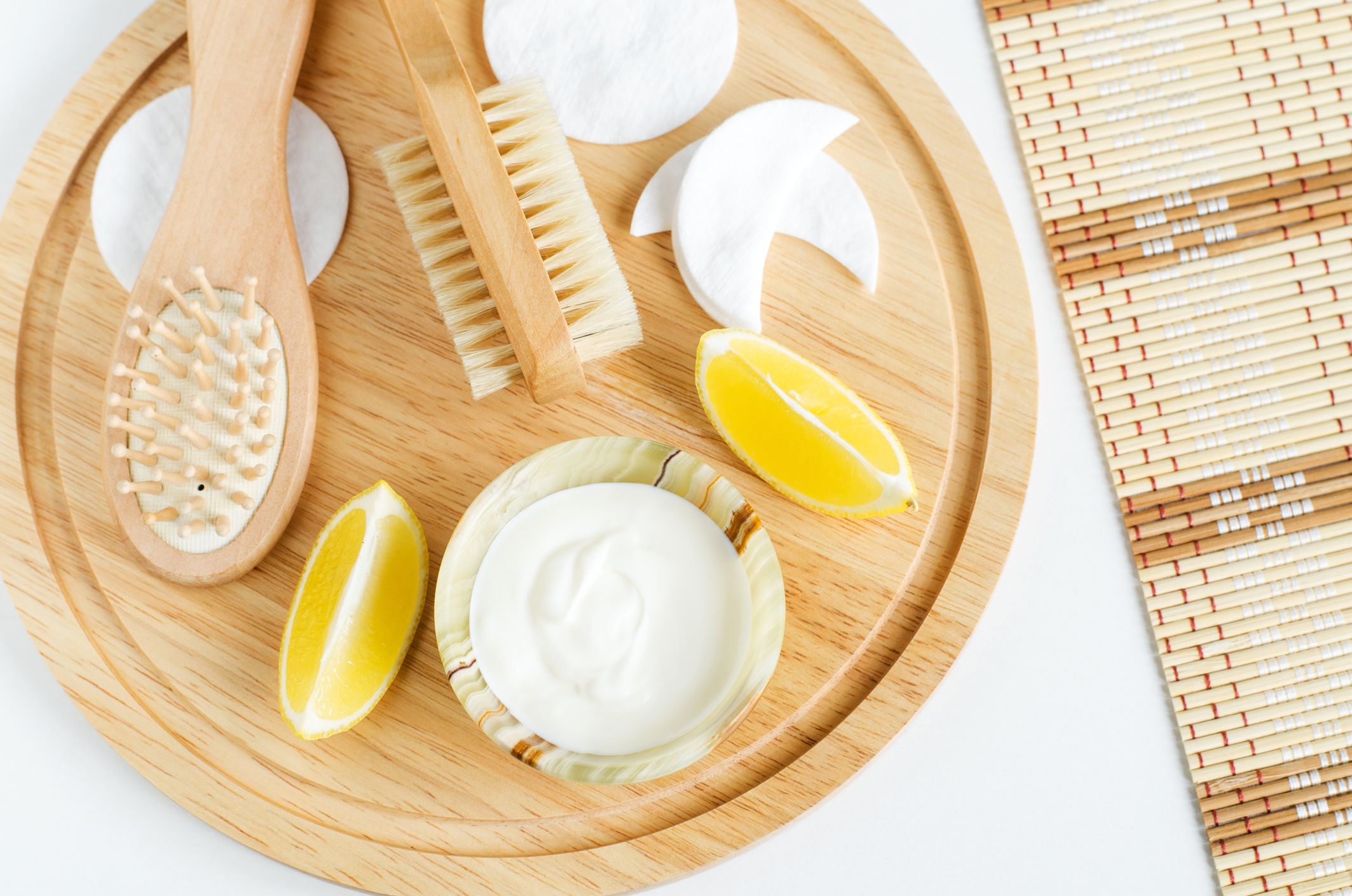 Fresh greek yogurt, lemon, cotton eye patches, wooden hair brush and body brush. Ingredients for preparing homemade face and hair masks. Natural skin care recipe and zero waste concept. Top view, copy space