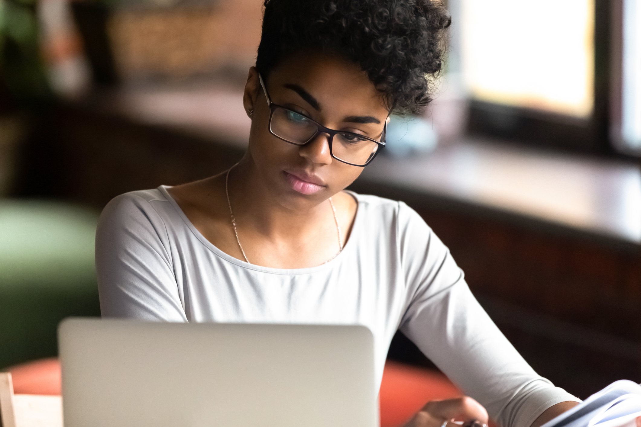 Thoughtful biracial girl in glasses focused studying on laptop