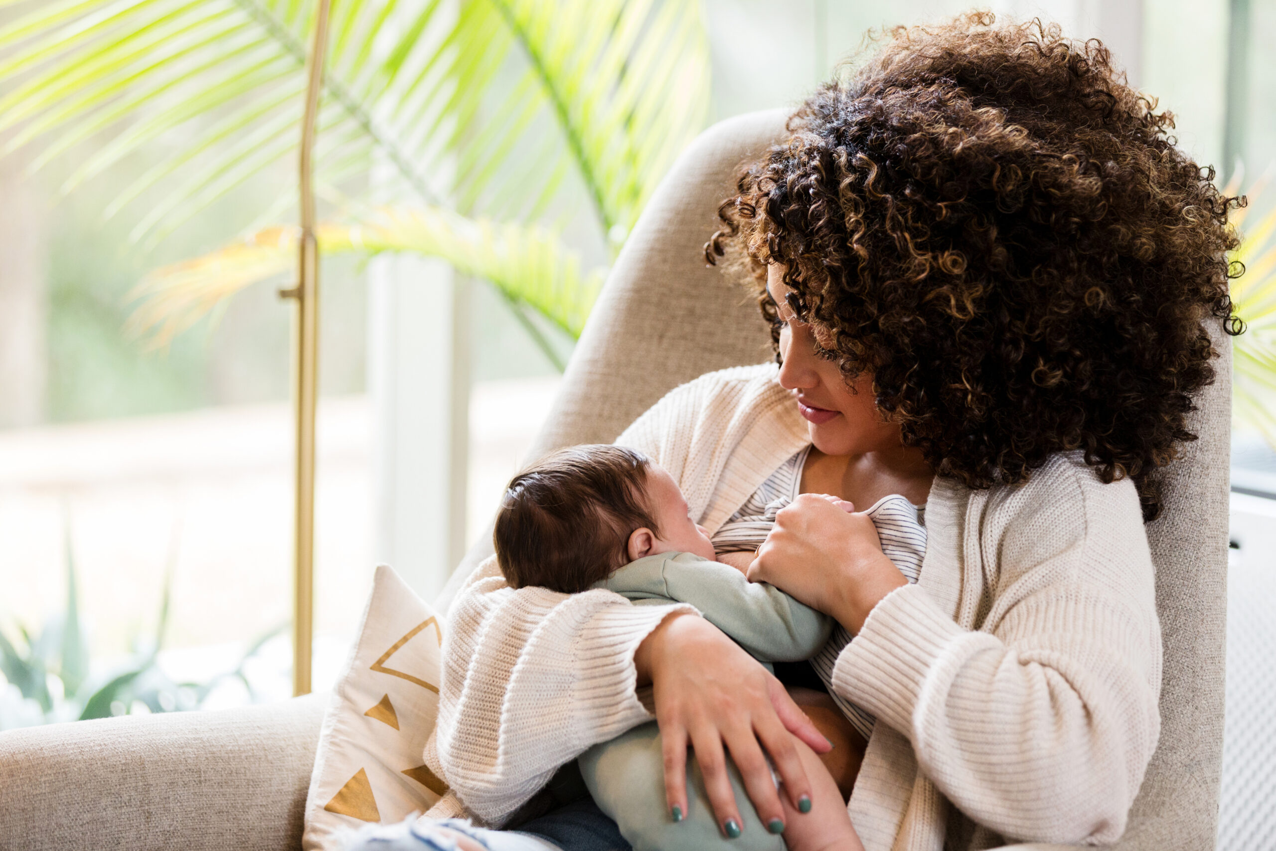 New mother breastfeeds baby in living room of home