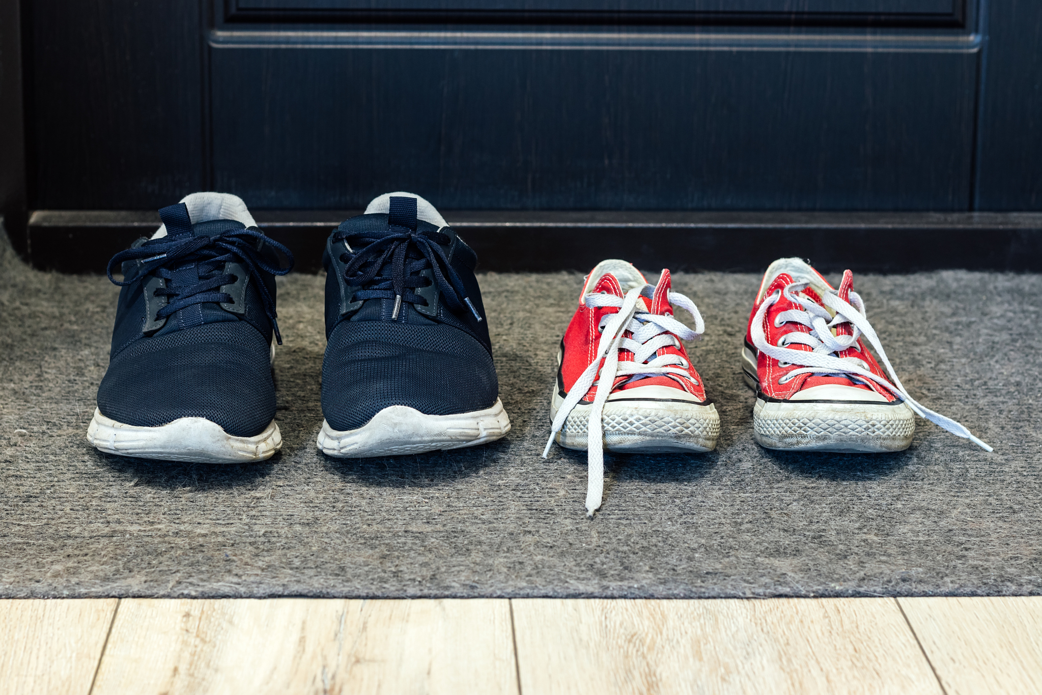 Family blue shoes and red sneakers on the rug at the front door. Closeup view