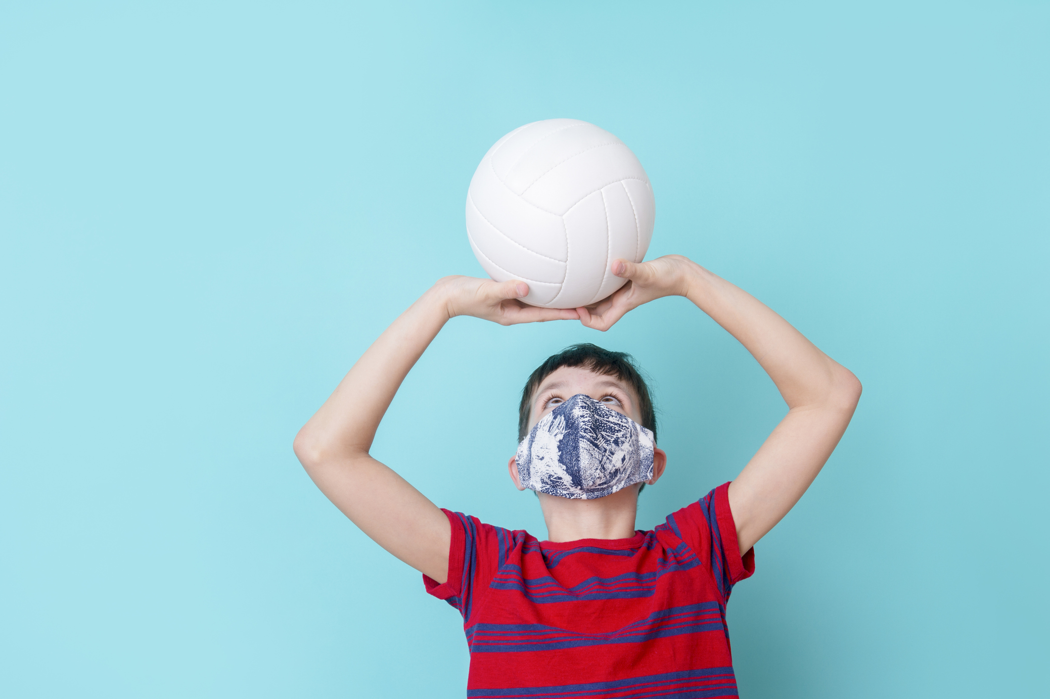 Boy with a mask due to the corona virus play volleyball on blue background. Workout online concept.