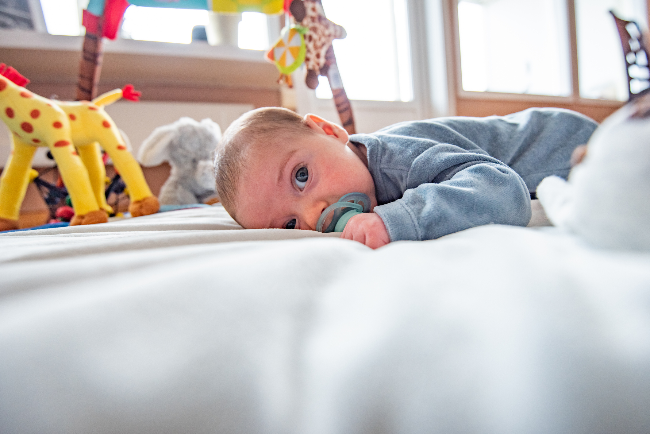 Cute baby boy on colourful gym, playing with hanging toys at home.