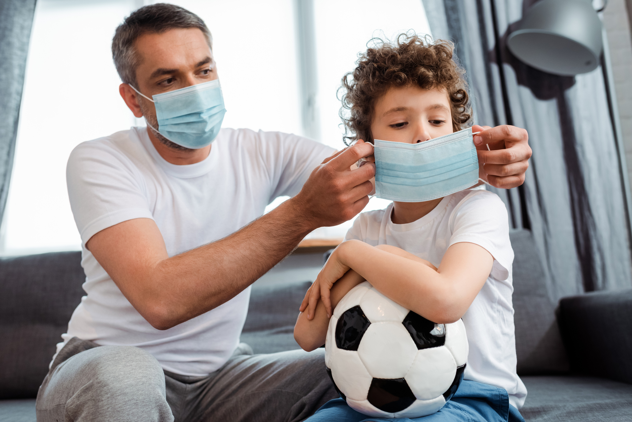 father wearing medical mask on curly son with football