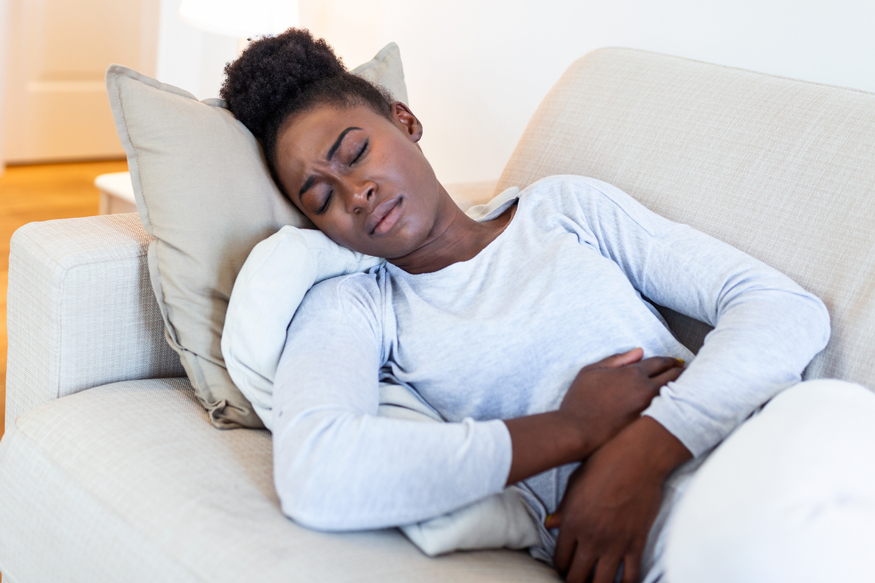 Woman in painful expression holding hands against belly suffering menstrual period pain, lying sad on home bed, having tummy cramp in female health concept