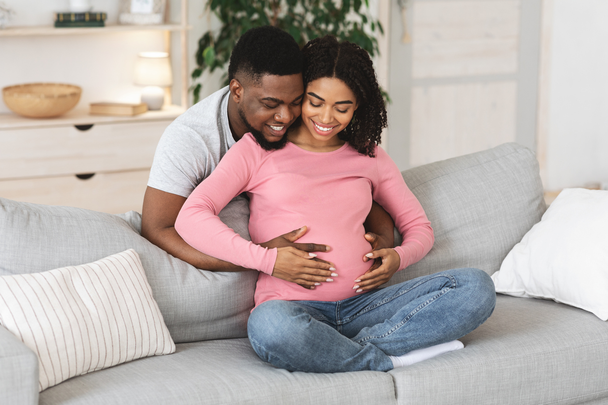 Joyful expecting african couple cuddling at home