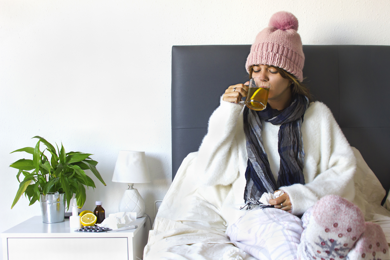 young woman laying in bed and drinking hot tea