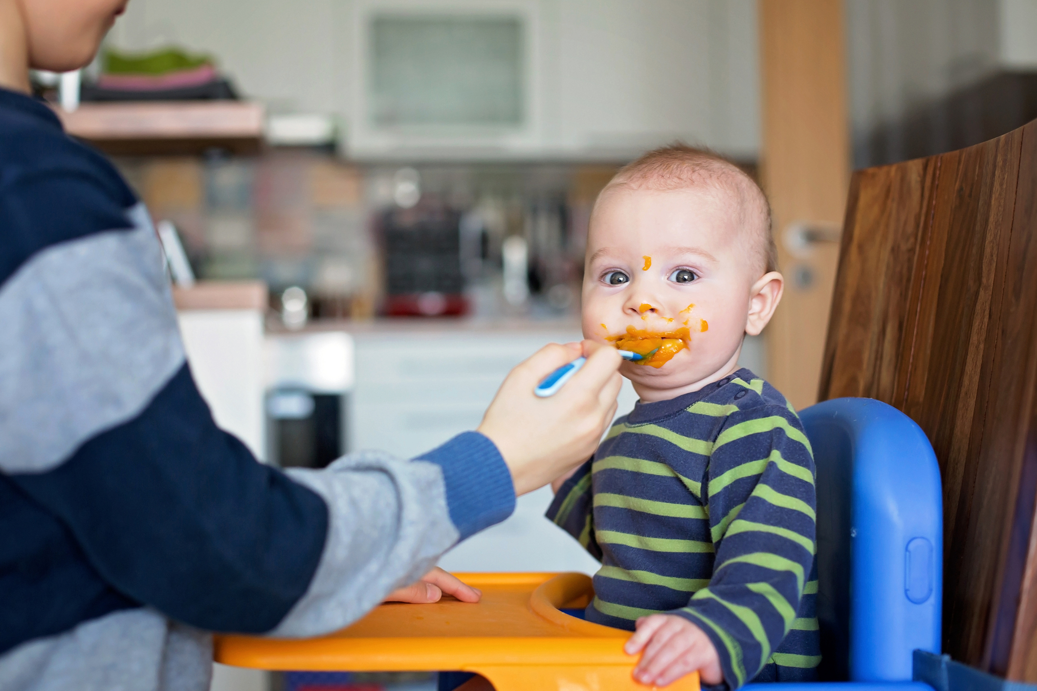 Cute preschool boy, feeding his baby brother with mashed vegetables, baby eating mashed food