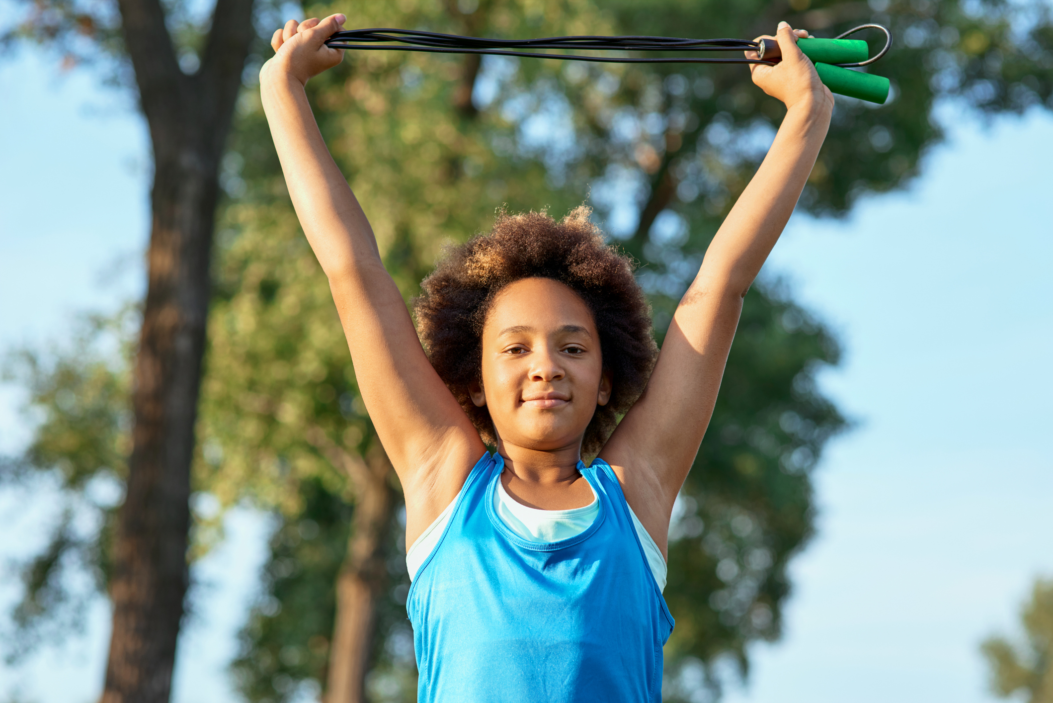 Cheerful little girl doing exercise with skipping rope outdoors