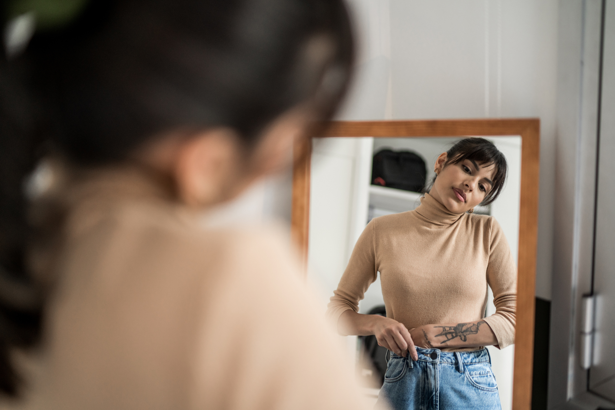 Young woman getting dressed in front of a mirror at home