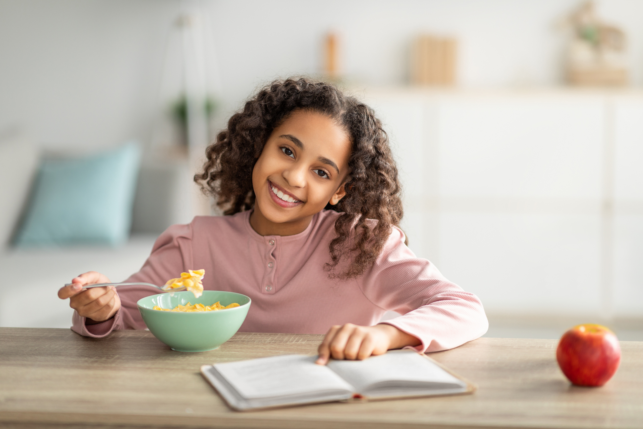 Morning routine concept. Cheerful black girl having healthy breakfast and reading book