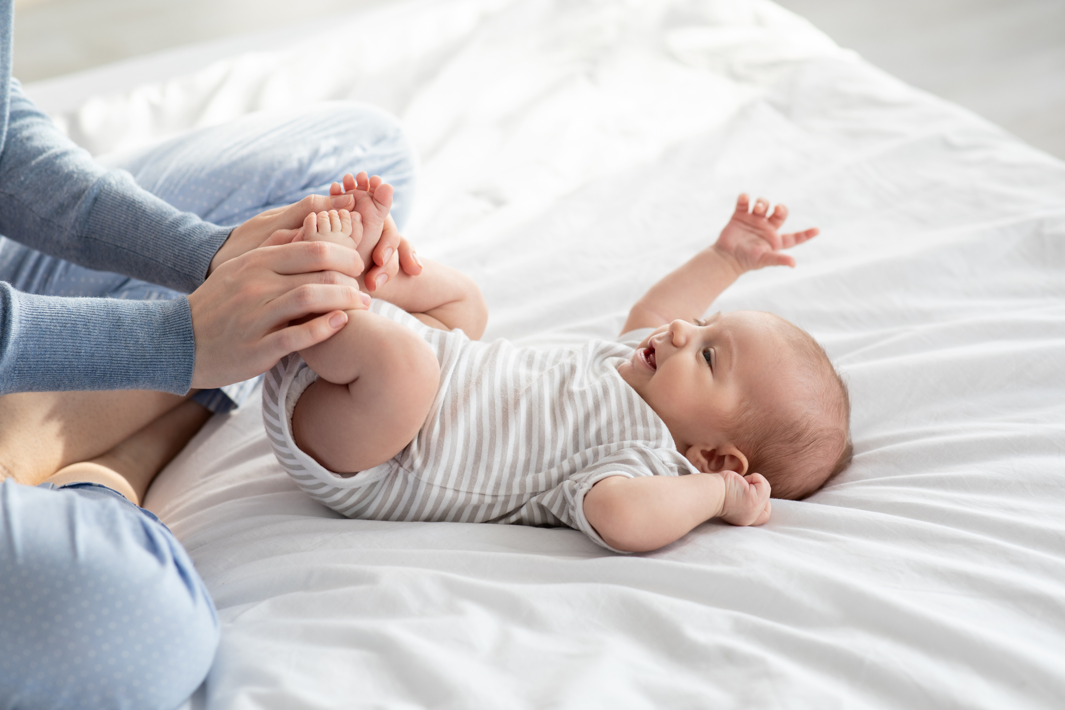 Caring Mother Making Gymnastics To Her Newborn Baby On Bed At Home