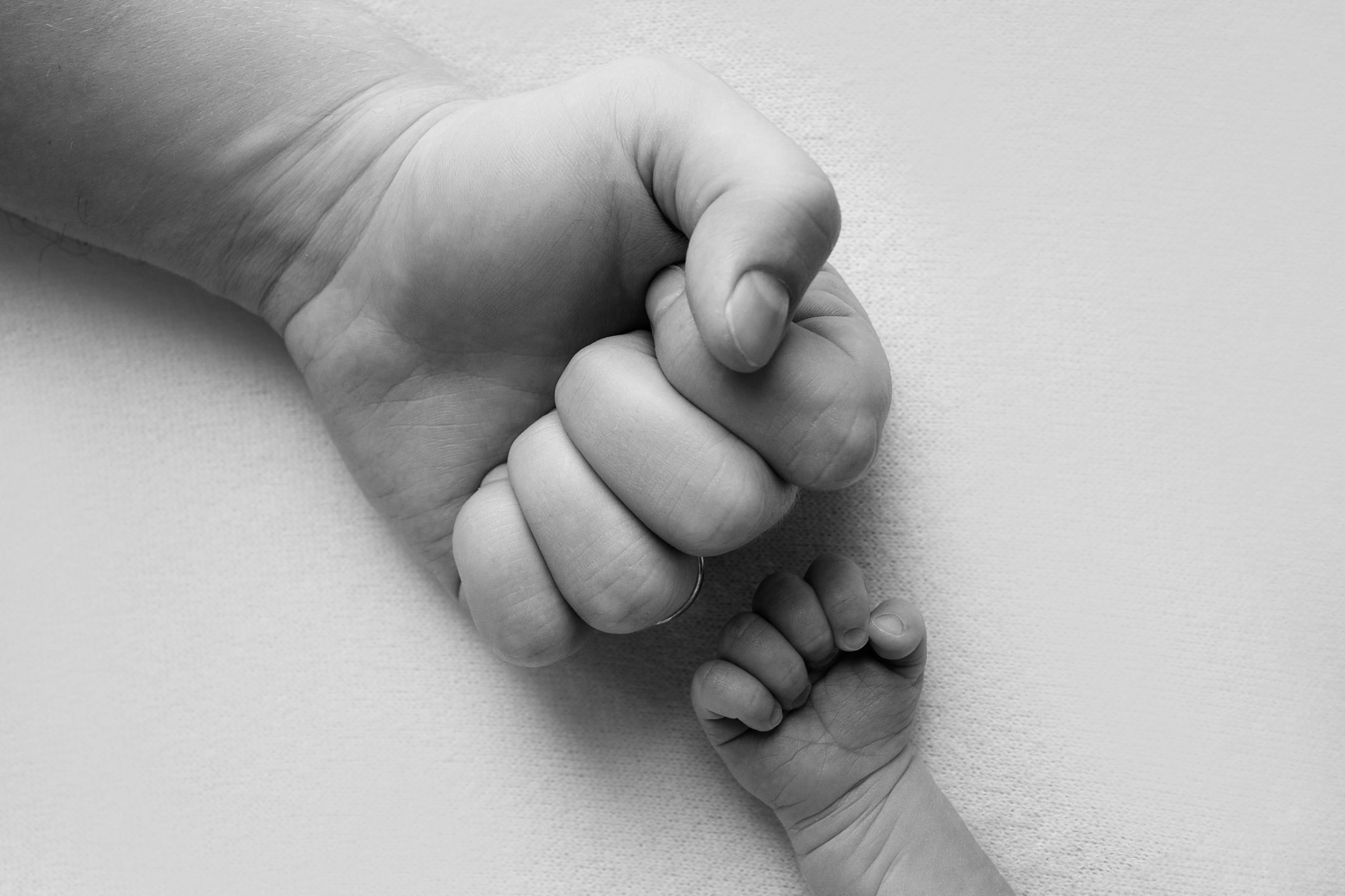 Dad and newborn boy son keep their hands in a fist, small and big fists. Father and son, the first boxing punch. Black and white photo.