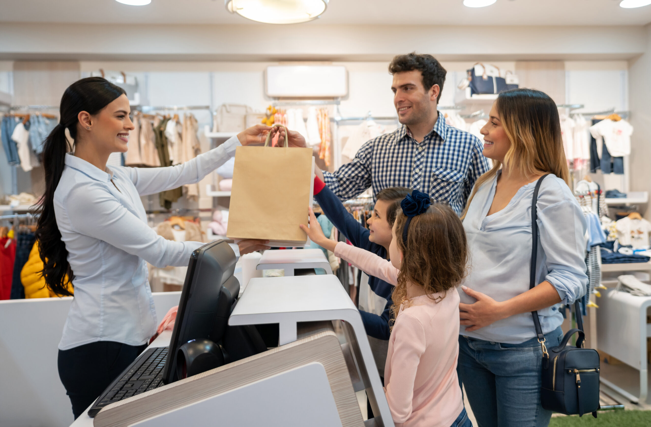 Happy family shopping at a kid's clothing store and paying to the cashier