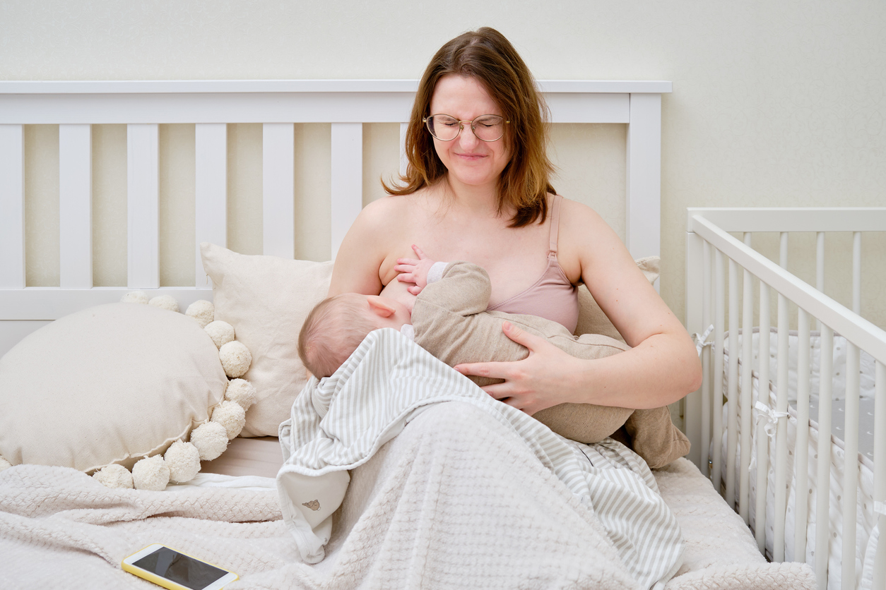 Pain and problems in a woman while breastfeeding a baby. Mother experiences discomfort while breastfeeding