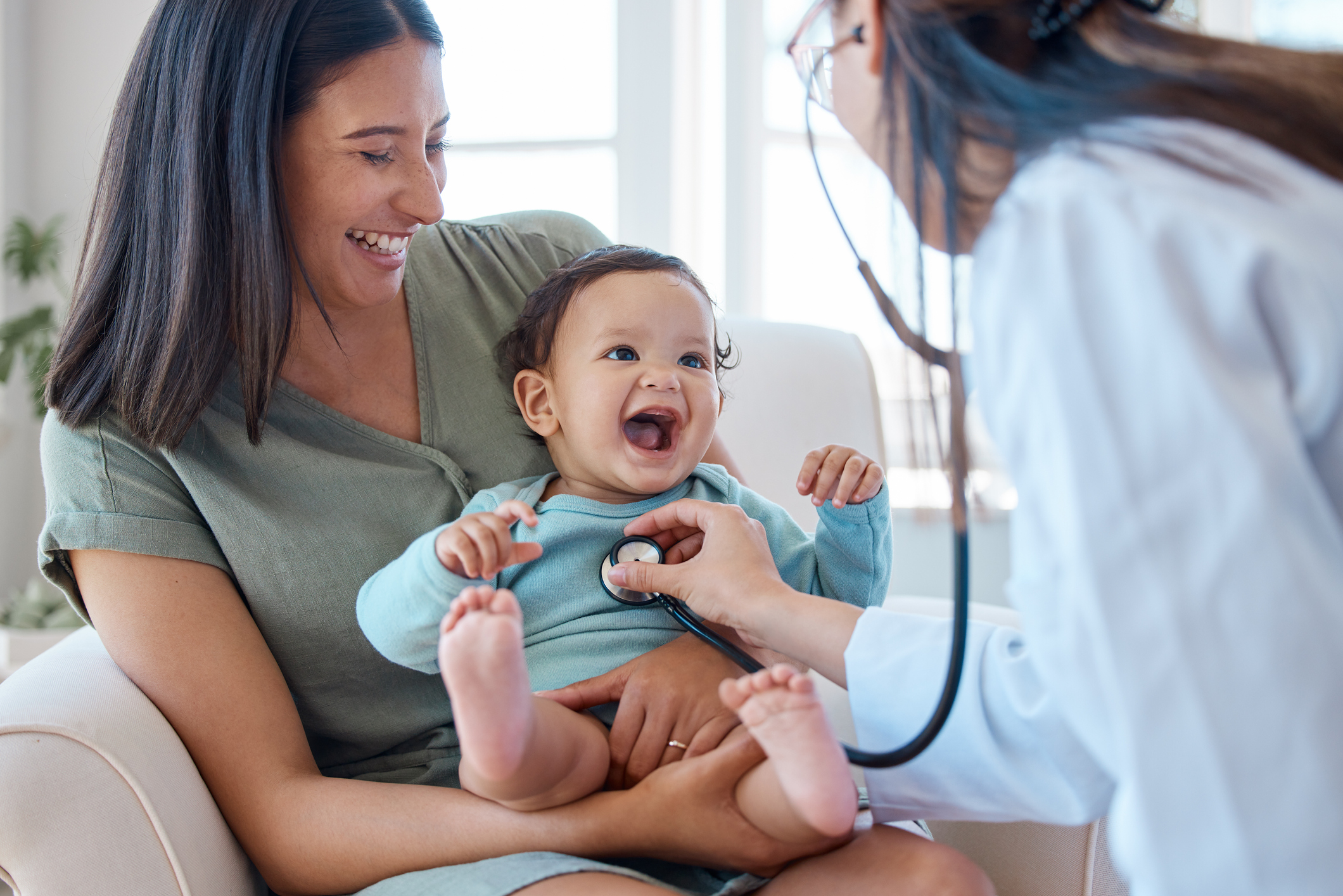 Shot of a baby sitting on her mother's lap while being examined by a doctor