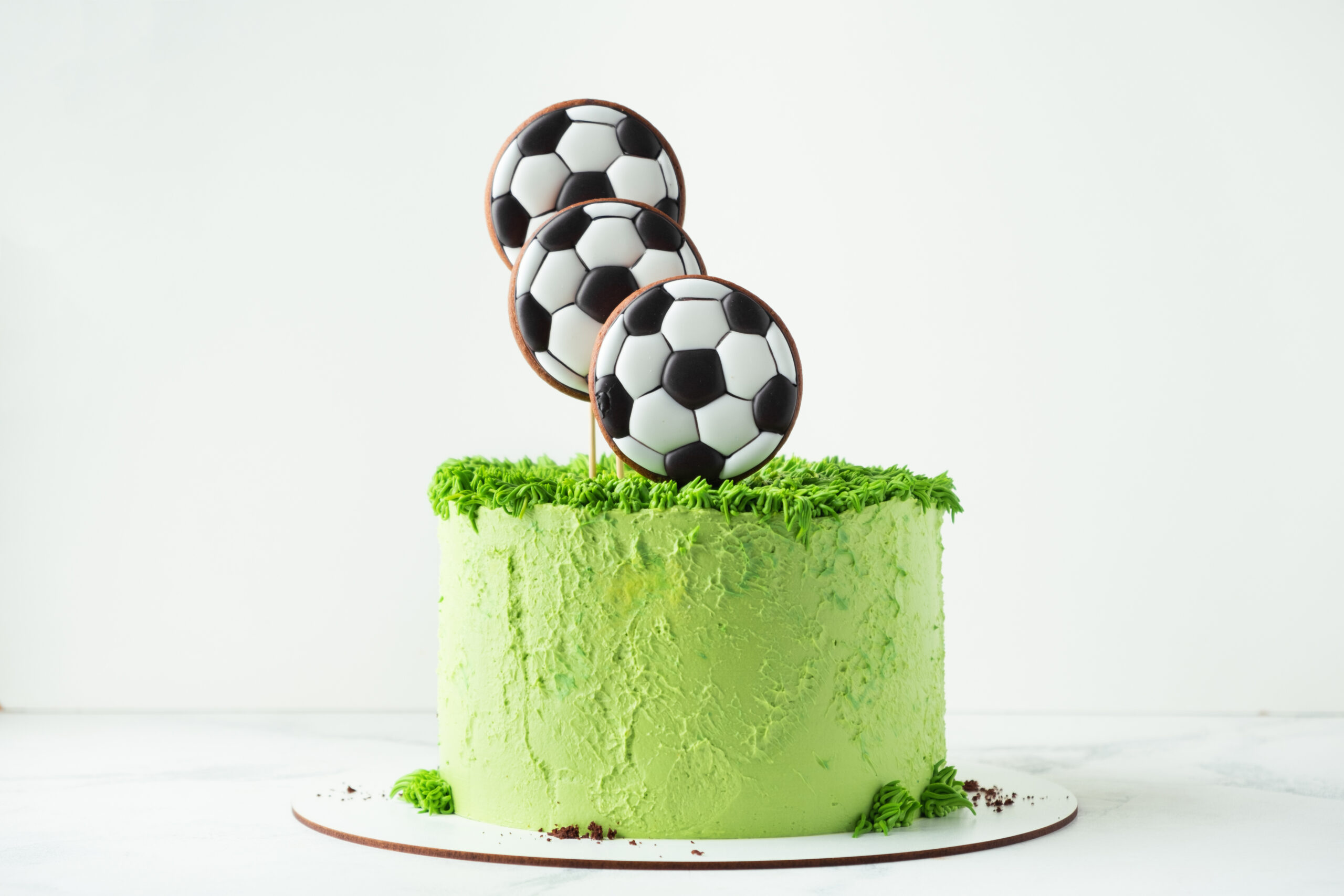 Birthday cake for a football fan with green cream cheese frosting, grass and soccer balls gingerbread cookies on top.