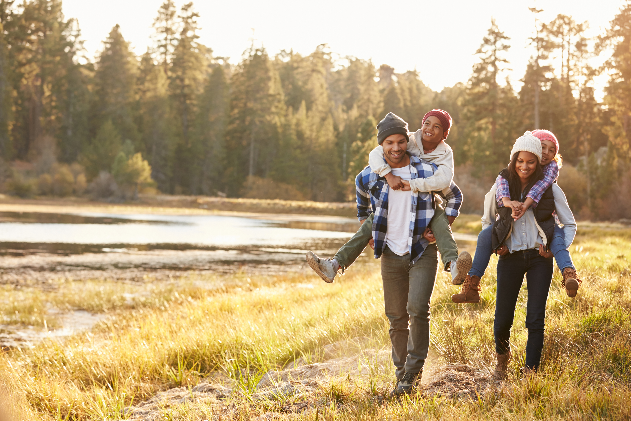 Parents Giving Children Piggyback Ride On Walk By Lake