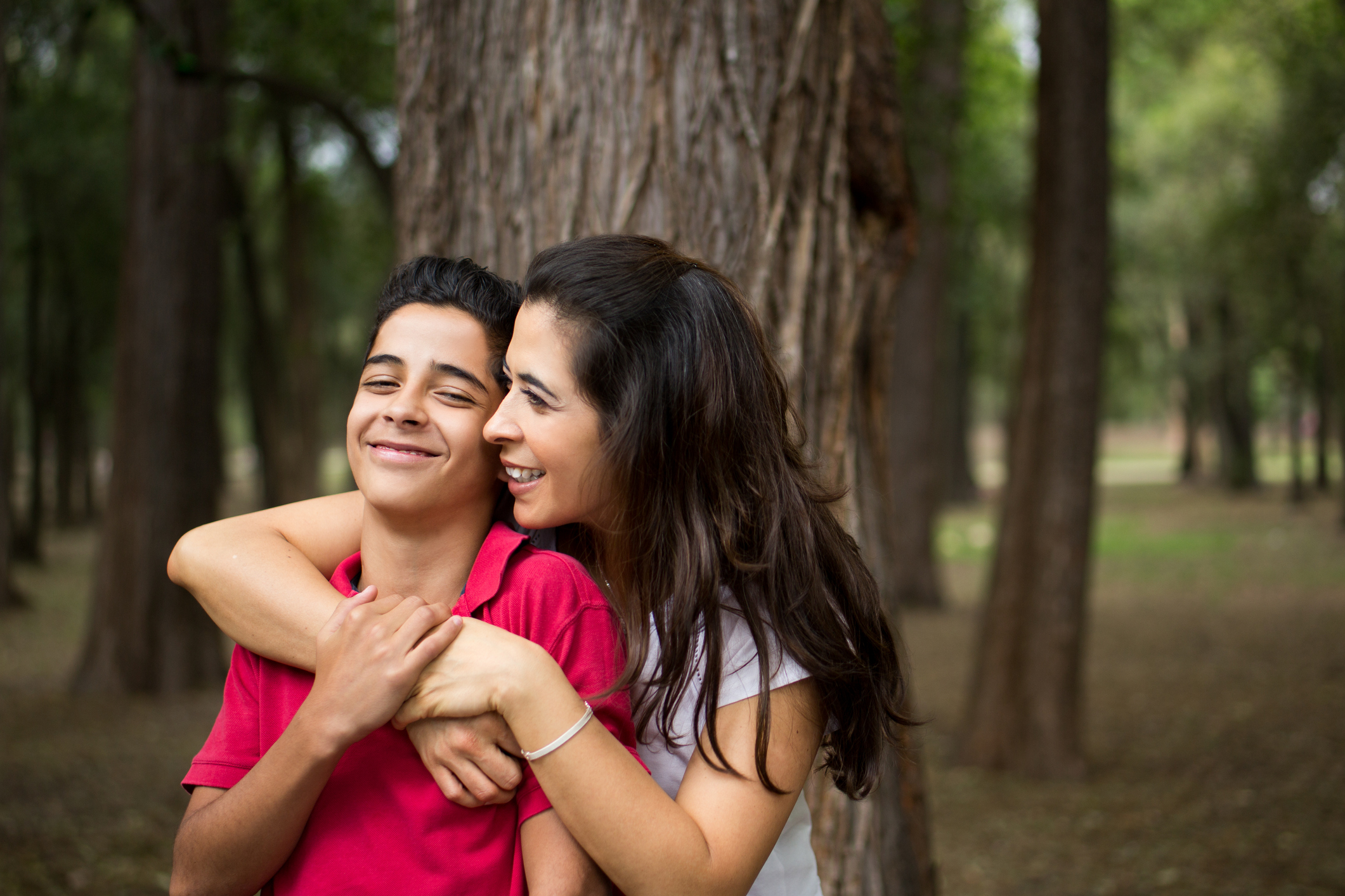 Affectionate latin mother embracing teen son and smiling