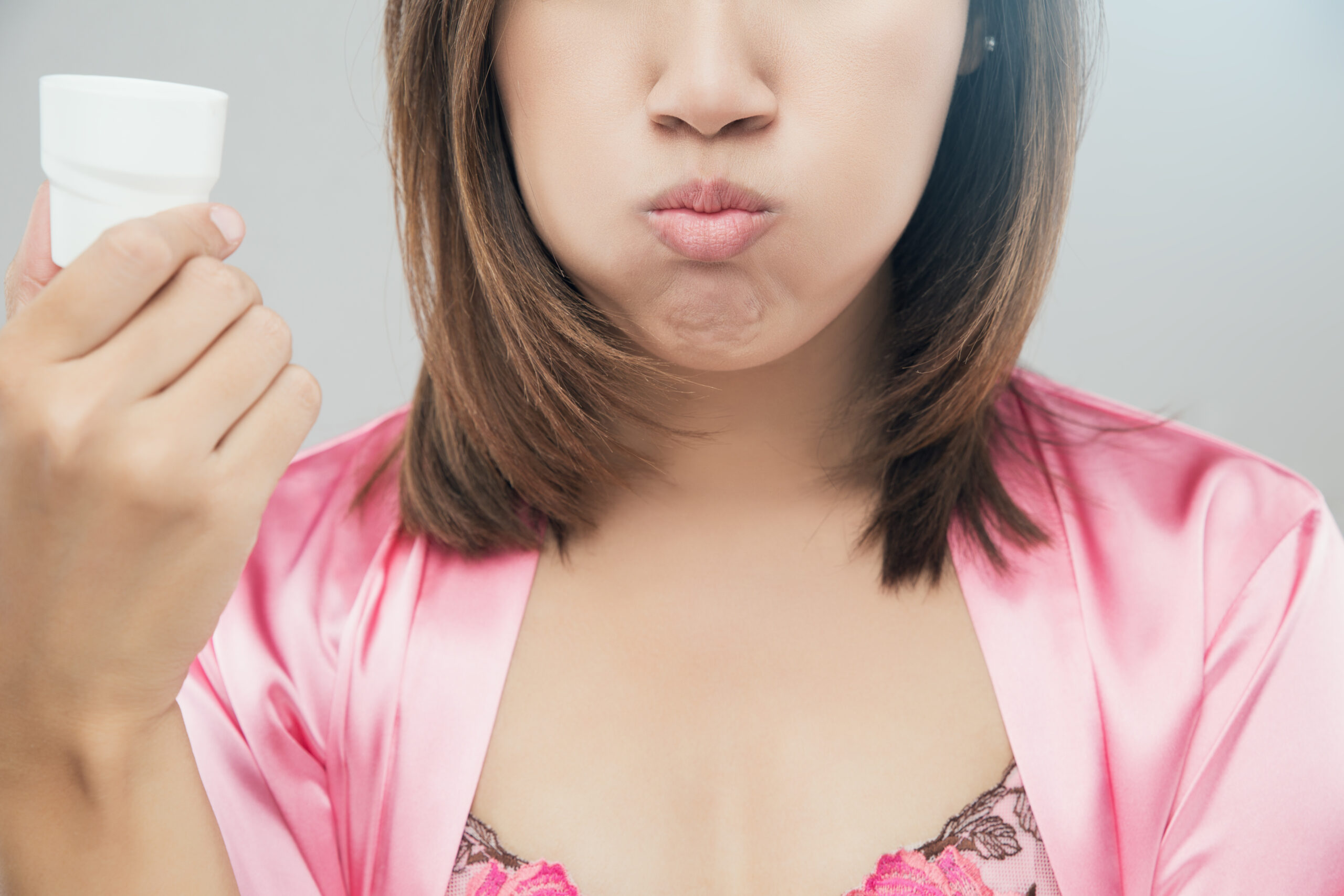 Woman rinsing and gargling while using mouthwash from a glass, During daily oral hygiene routine, Girl in a pink silk nightwear, Dental Healthcare Concepts