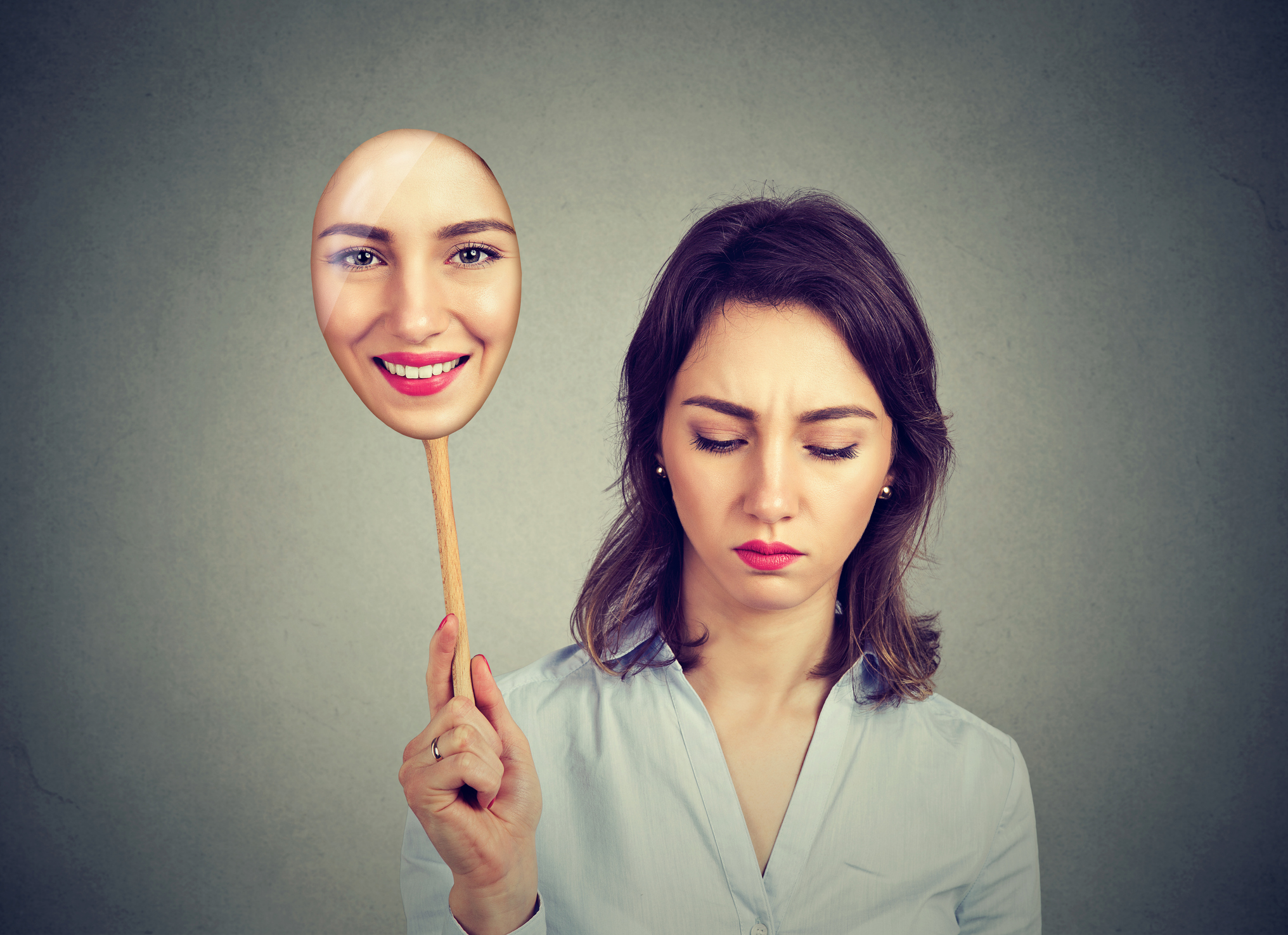 Sad woman looking down taking off happy mask of herself