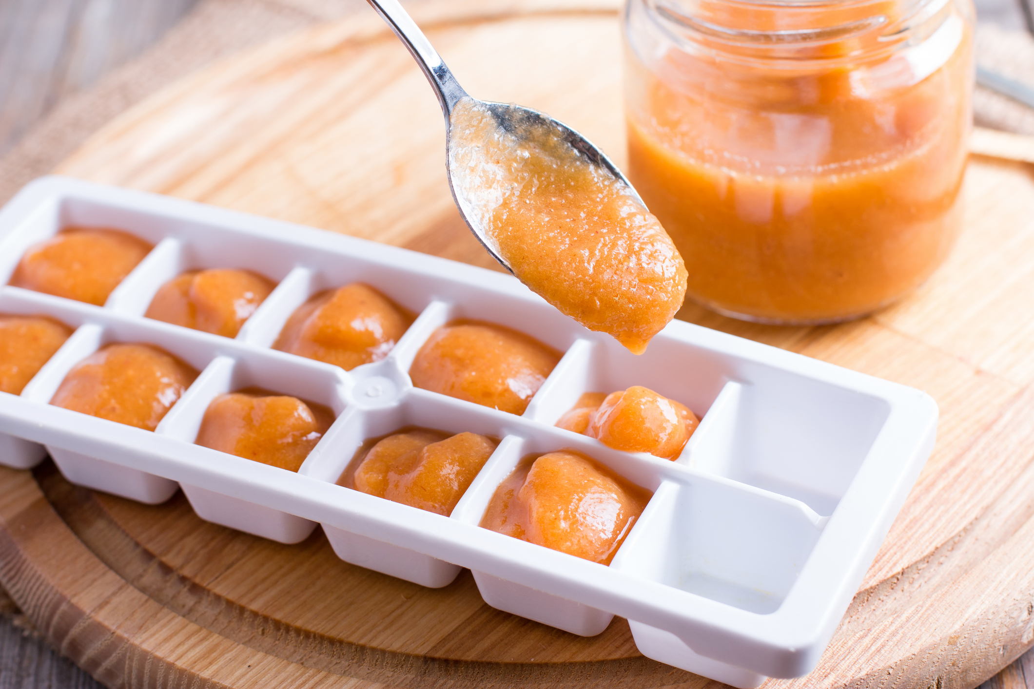 Ice tray with fresh fruit puree on wooden background