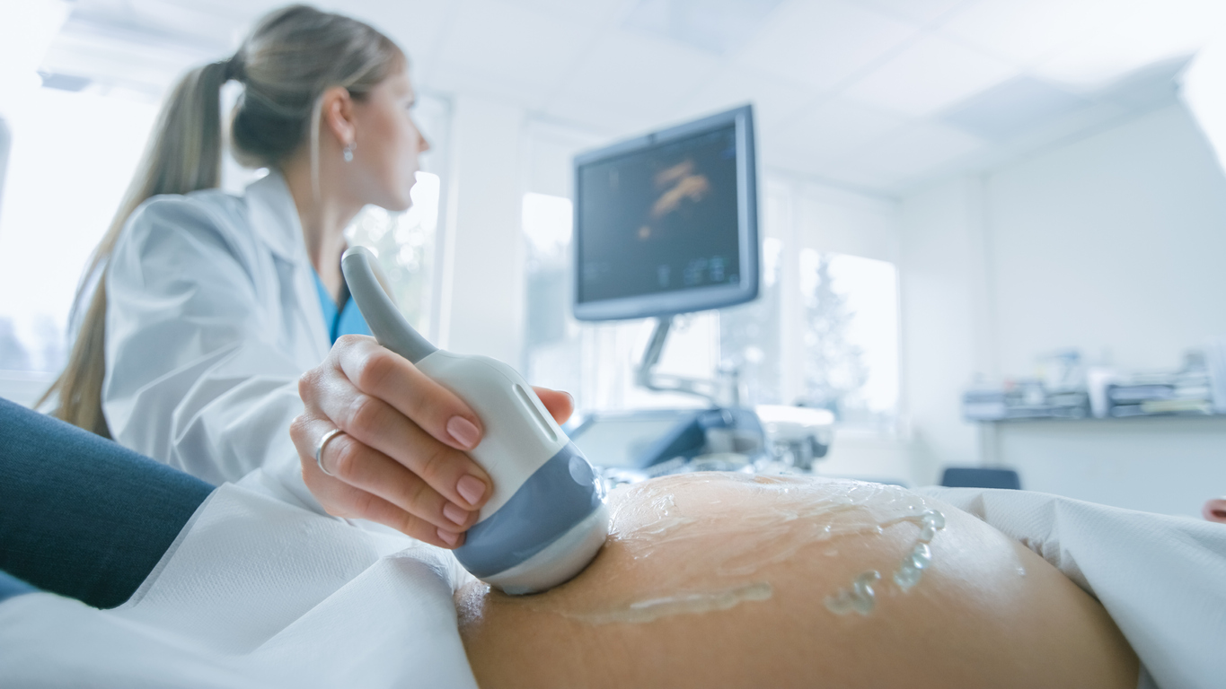 In the Hospital, Close-up Shot of the Doctor does Ultrasound / Sonogram Procedure to a Pregnant Woman. Obstetrician Moving Transducer on the Belly of the Future Mother.