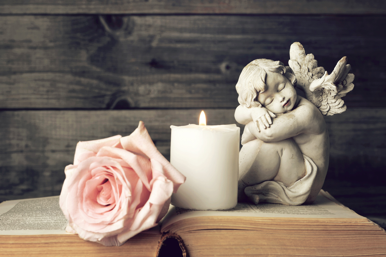 Angel, candle and pink rose on wooden background