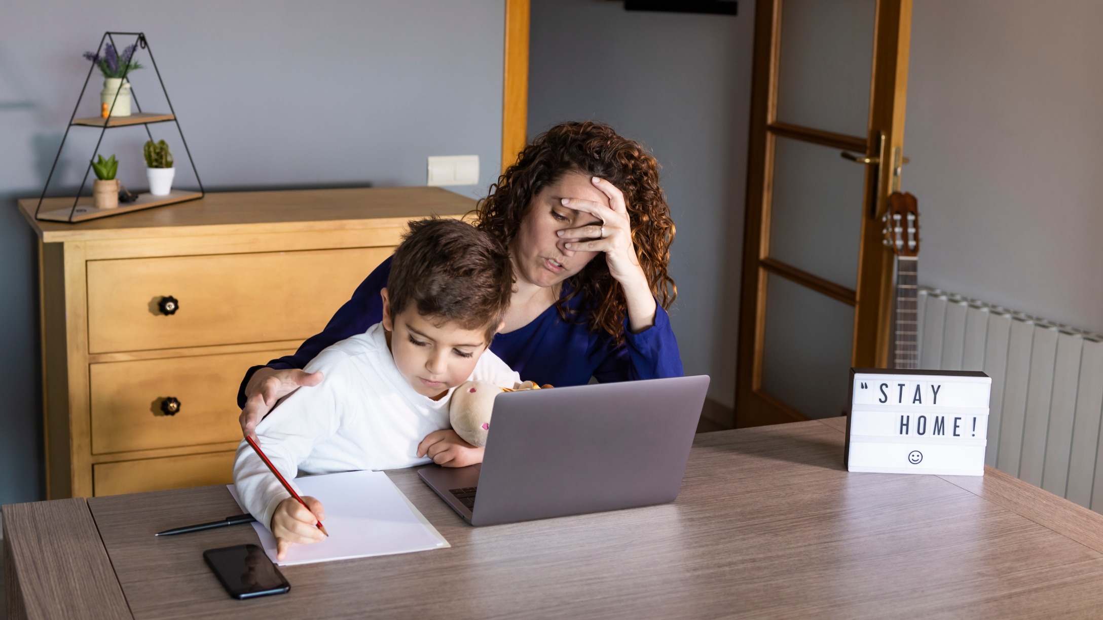 Mamá estresada frente a computadora con hijo