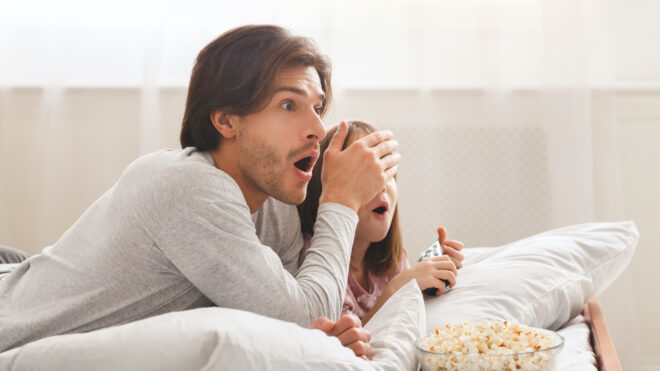 parent watching TV and covering child's eyes