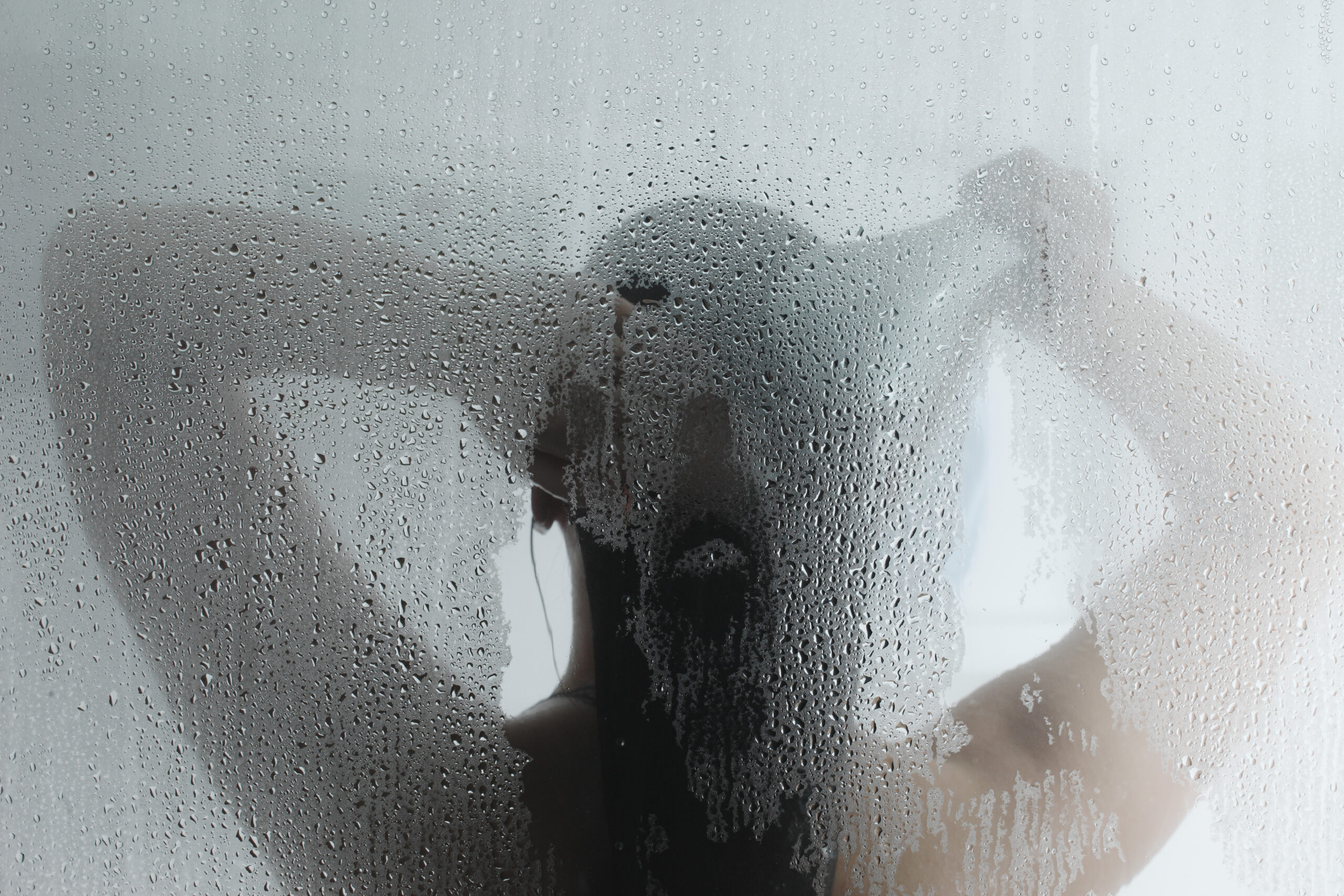 Silhouette of woman taking shower behind steamy door