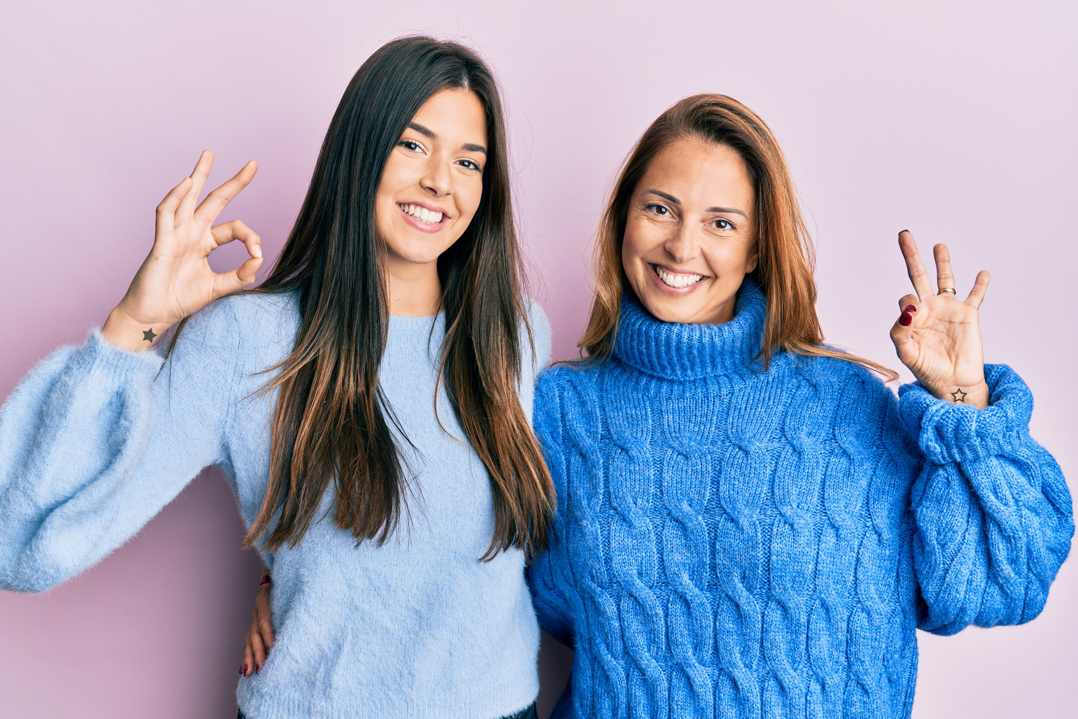 Hispanic family of mother and daughter wearing wool winter sweater smiling positive doing ok sign with hand and fingers. successful expression.