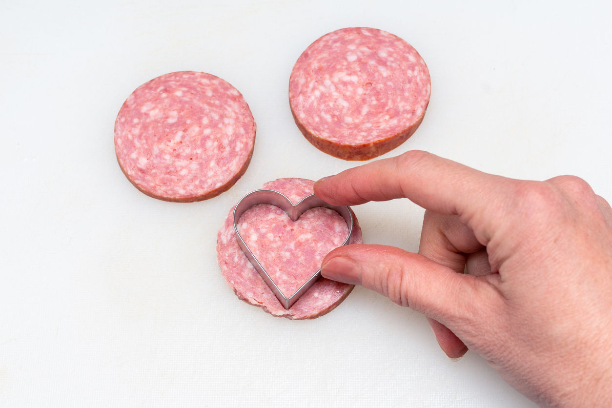 A woman's hand cuts a sausage, salami, bacon, top view, close-up. Cooking a festive breakfast at home